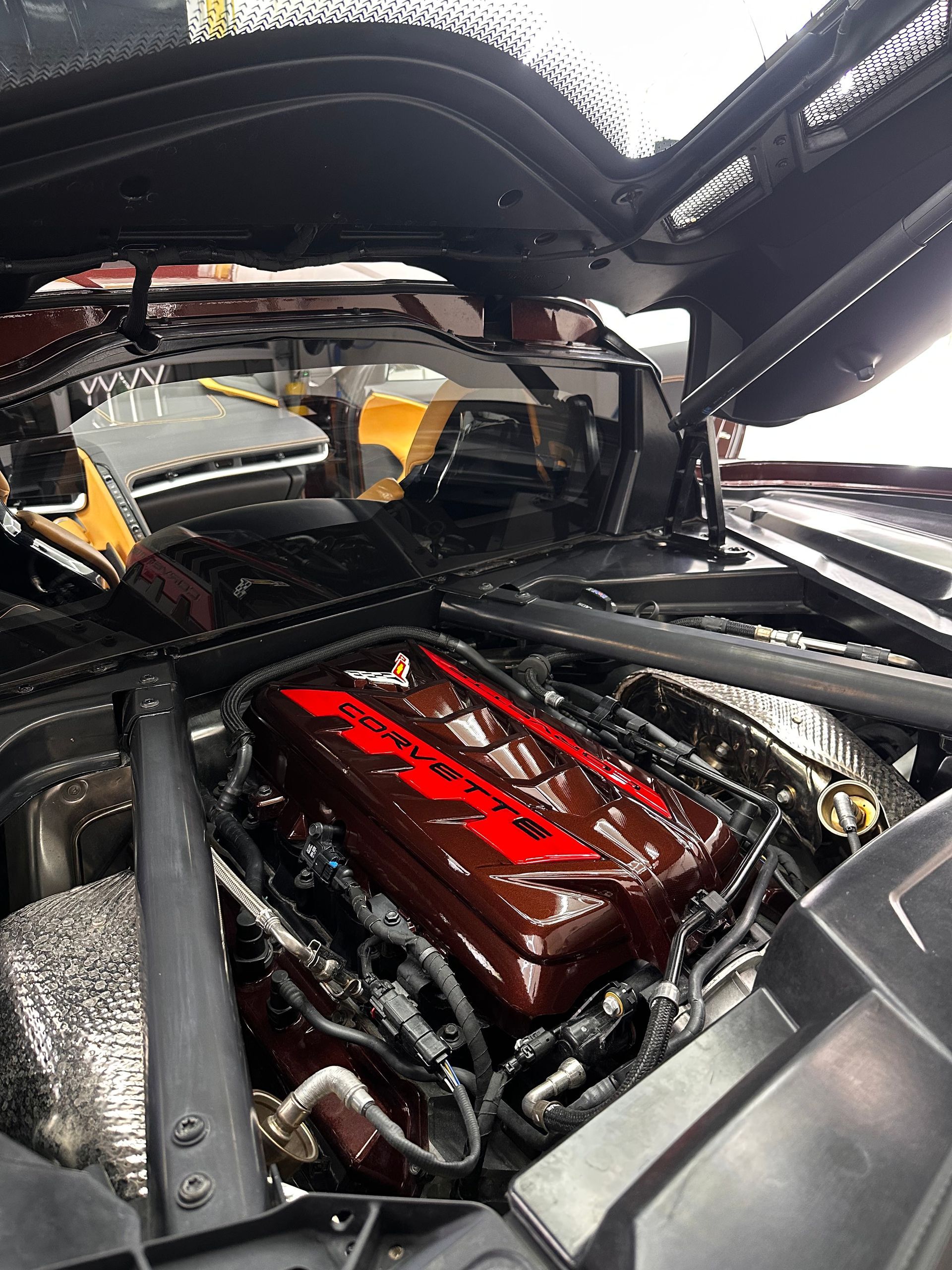 Car engine bay with glossy red valve cover under an open hood, showing polished custom components