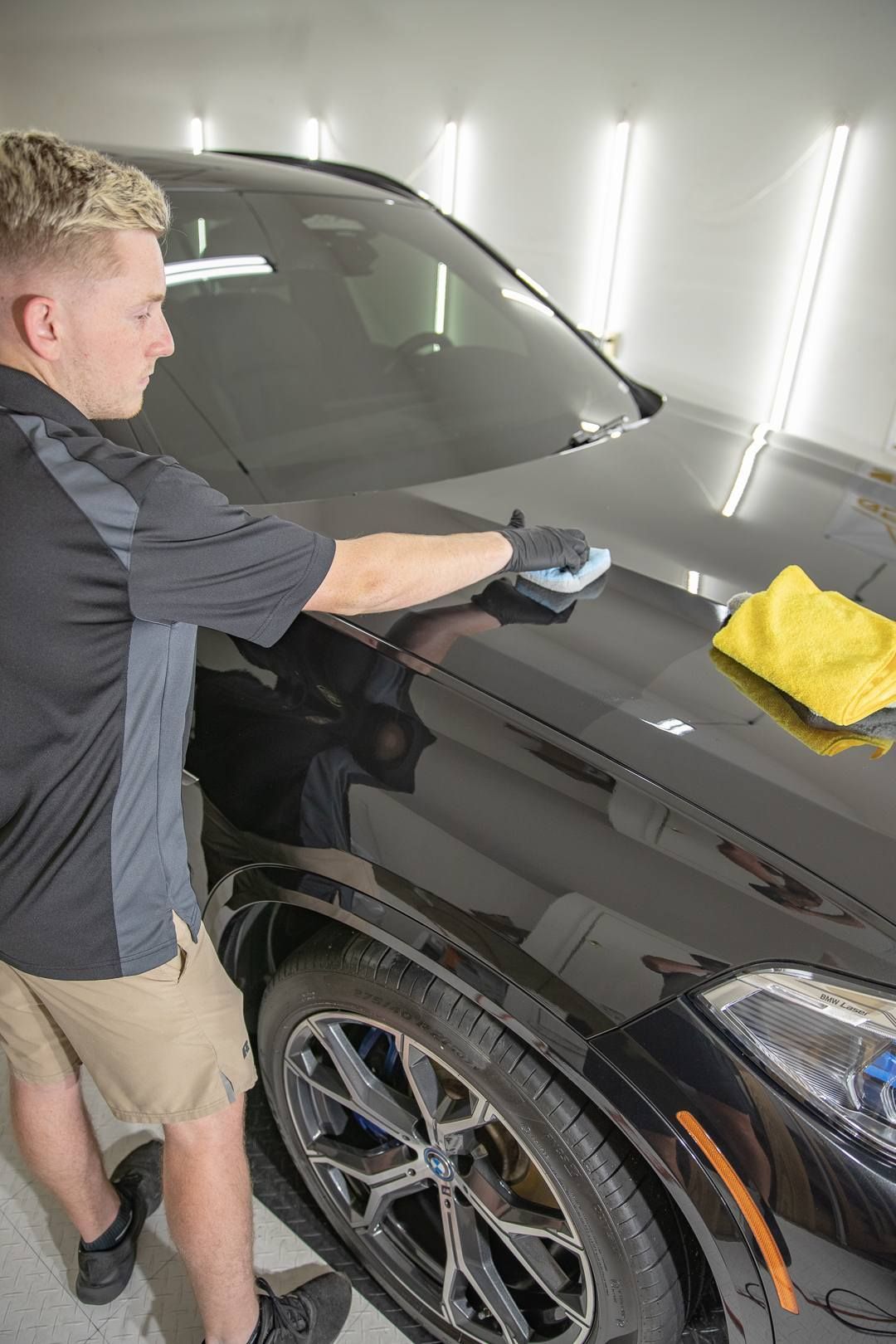 Person wiping a black SUV hood with a cloth in a garage detailing bay