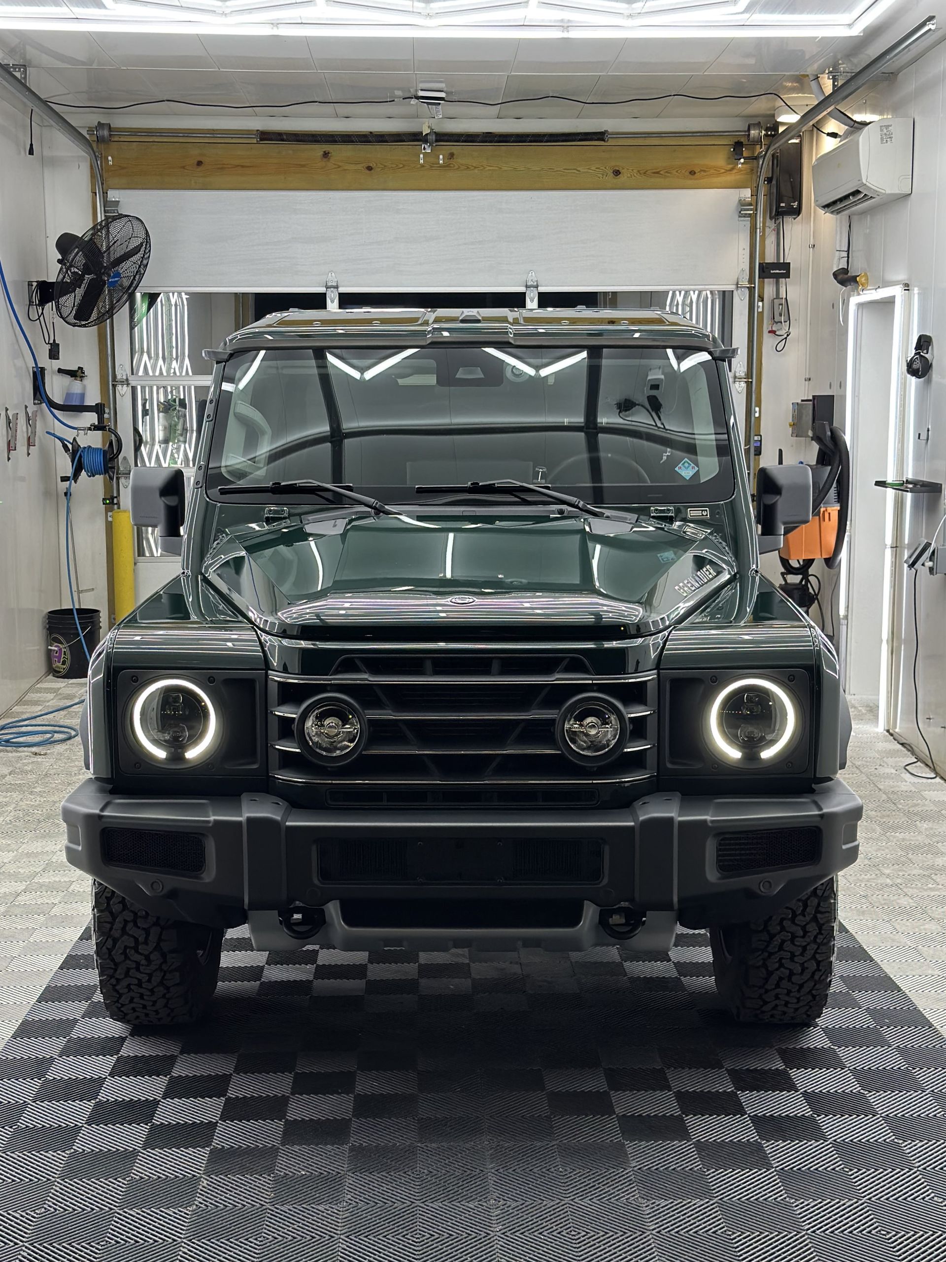 Dark green SUV with round headlights parked indoors, in a car wash bay.