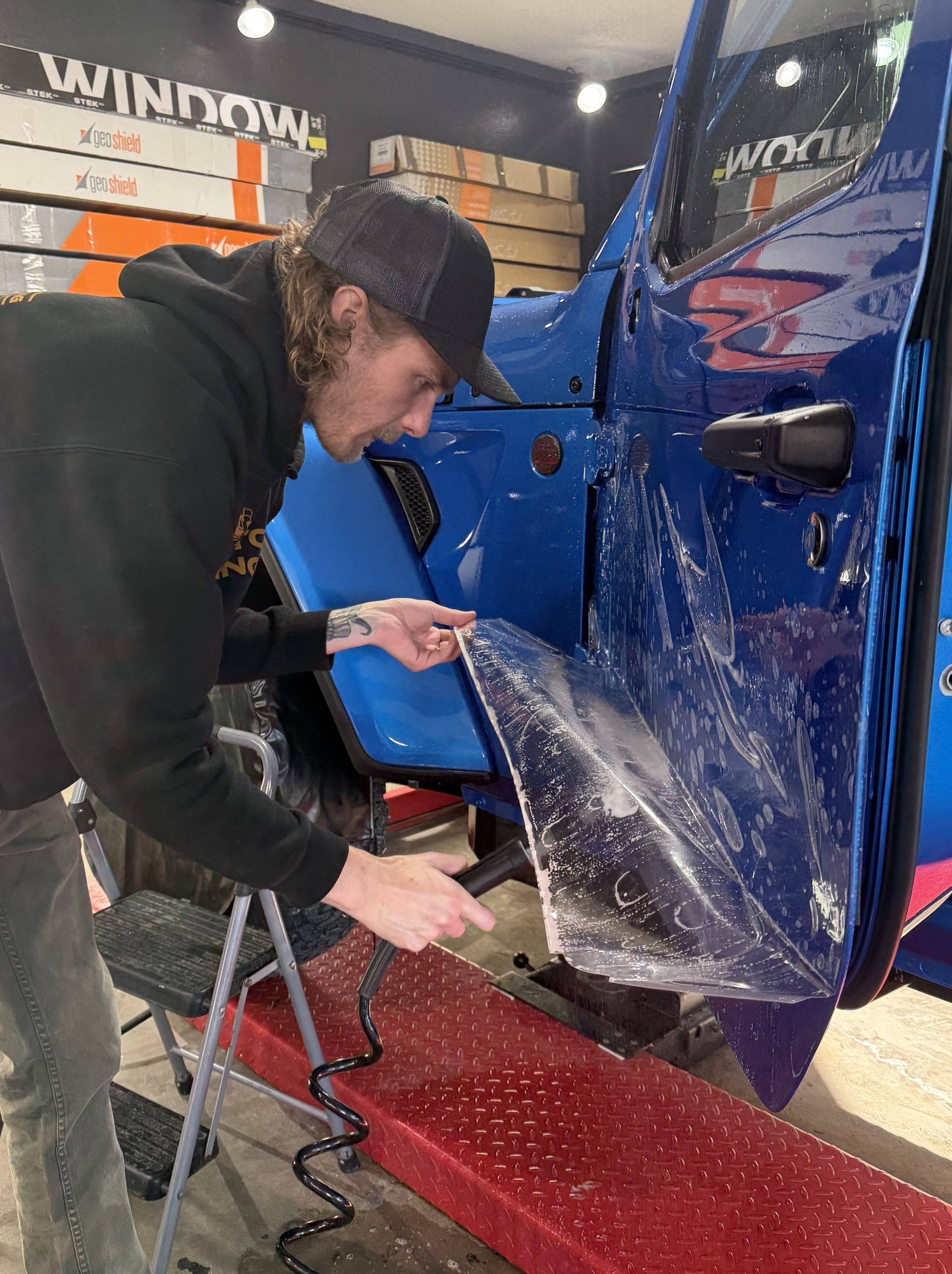 Person cleaning the inside of a blue car door in an auto detailing shop