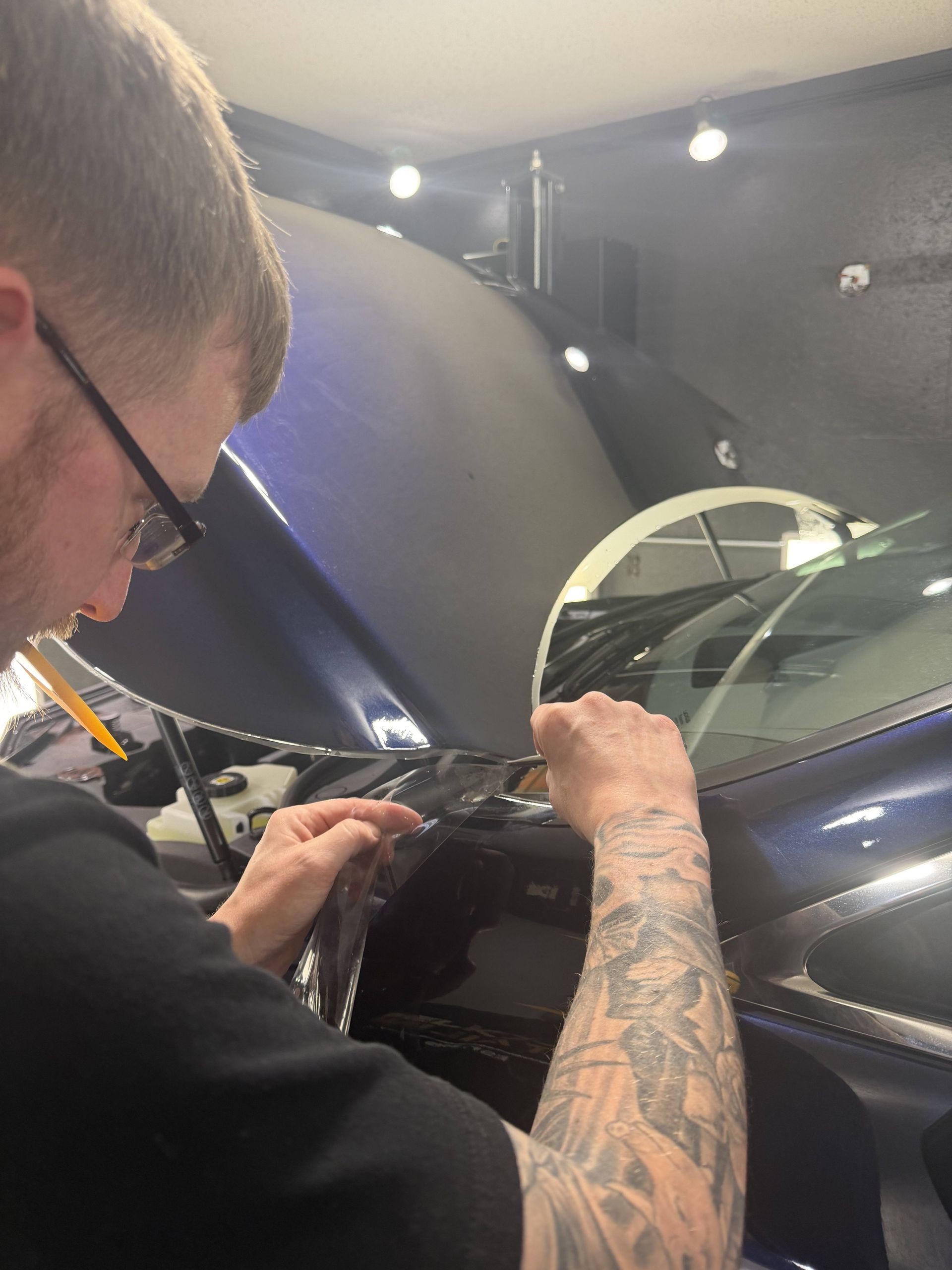 Person working on a blue car’s dashboard in a garage with the driver’s door open