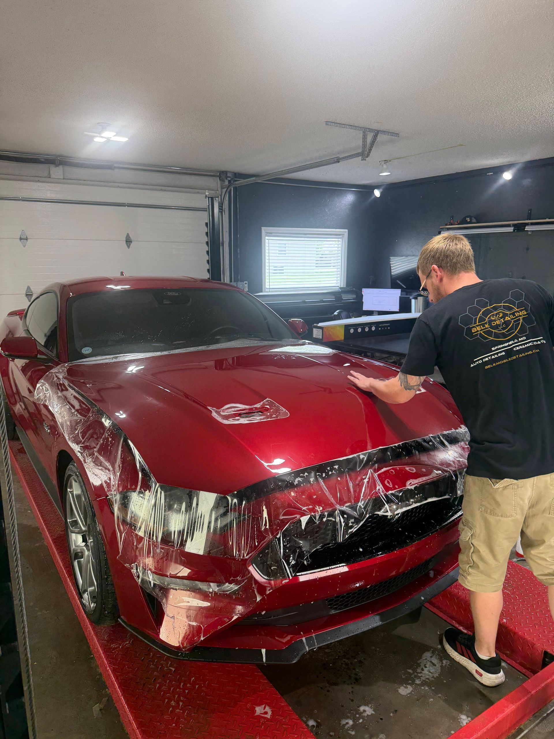 Red sports car with front-end damage in a garage, with a man working beside it.