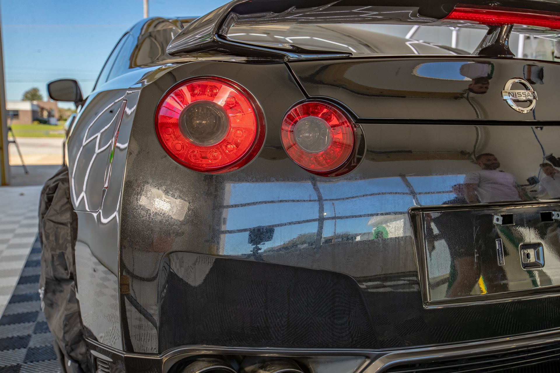 Black Nissan GT-R sports car rear with circular red tail lights, glossy finish, parked indoors with reflections.