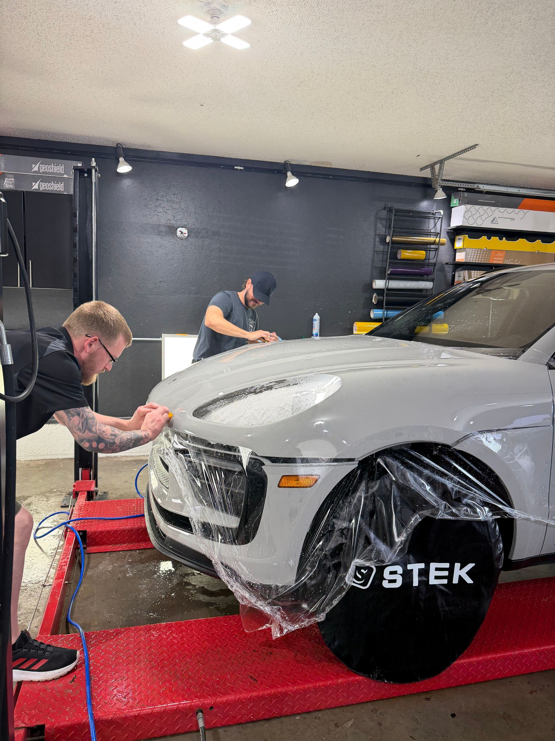 Two people washing a white Mercedes-Benz SUV in front of a brick building.