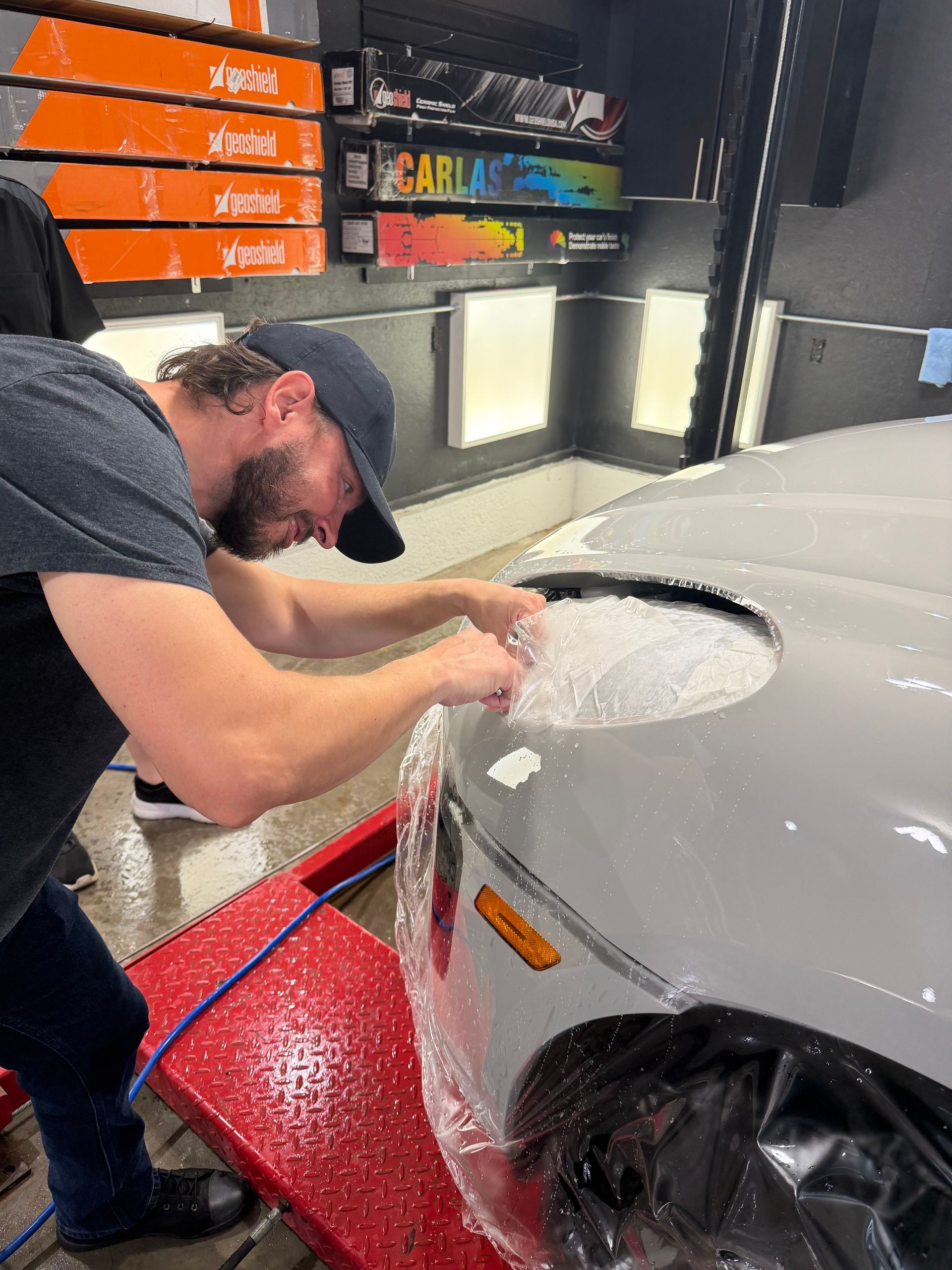 Man polishing a white car in a garage, with soapy water and detailing supplies on shelves.