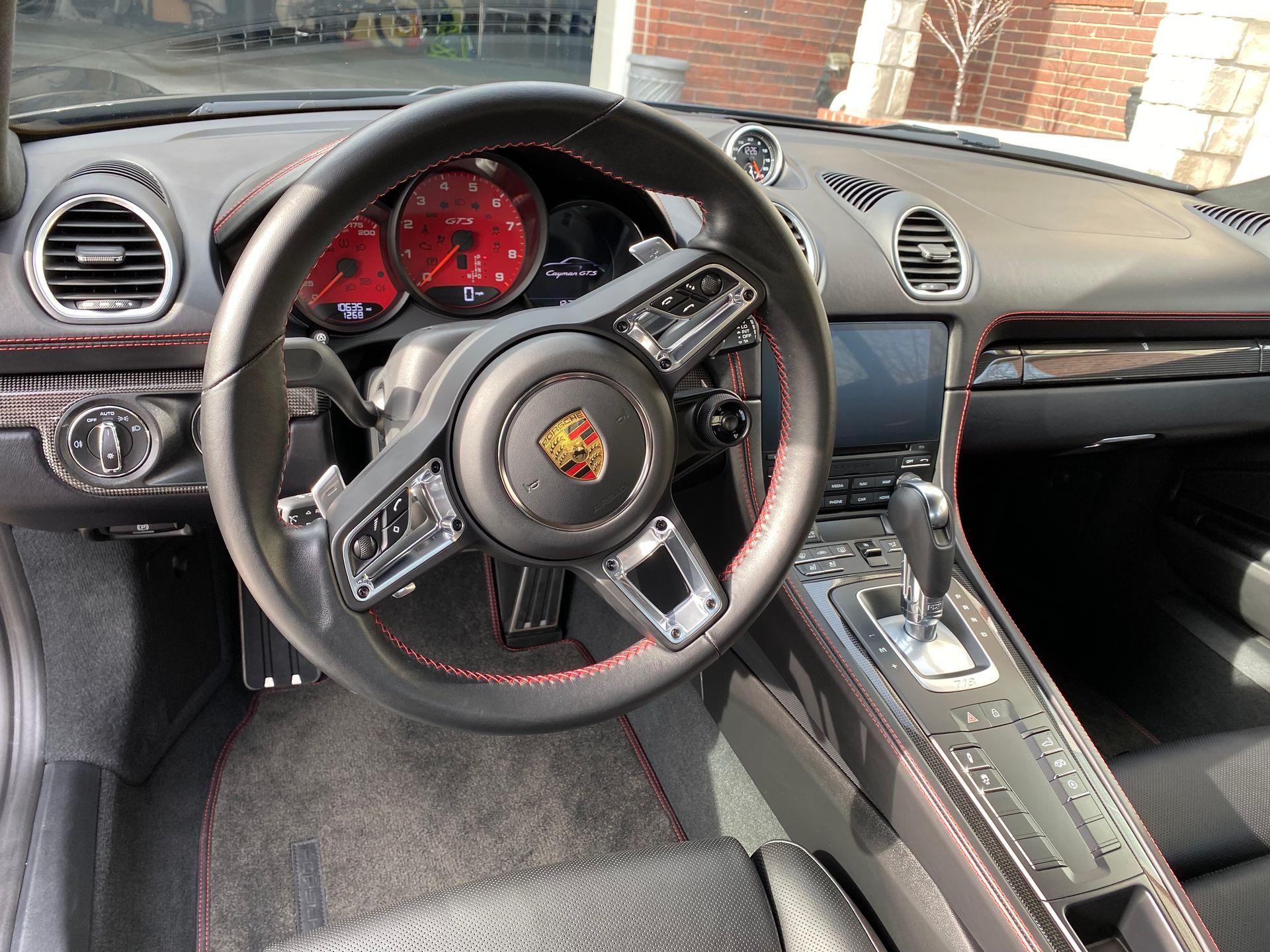 Interior of a Porsche sports car, showing the steering wheel, red gauges, dashboard, and center console.