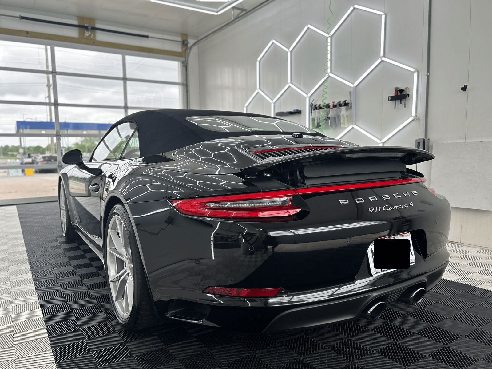 Black Porsche convertible in a showroom, rear view with hexagonal wall lights and large windows.