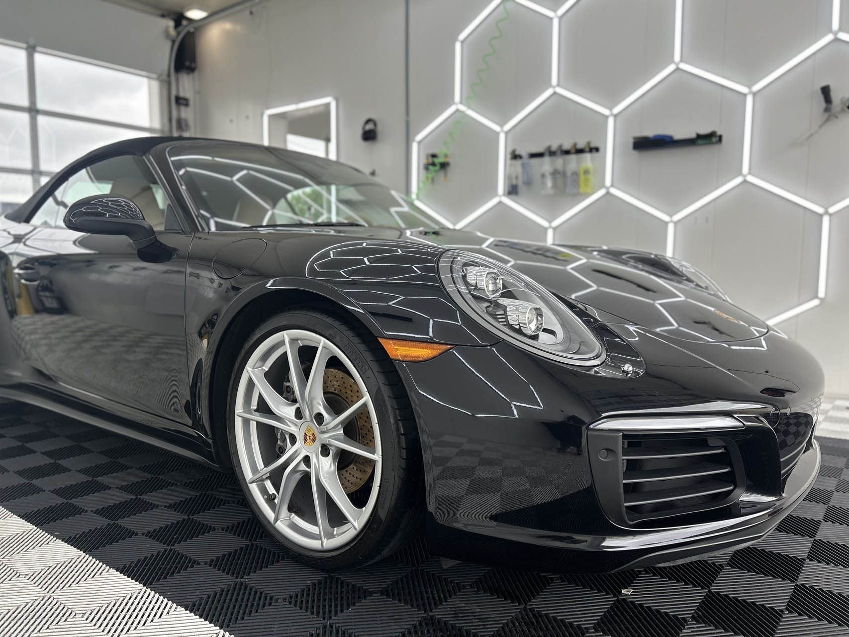 Black sports car in a showroom with hexagonal wall lights and a checkered floor