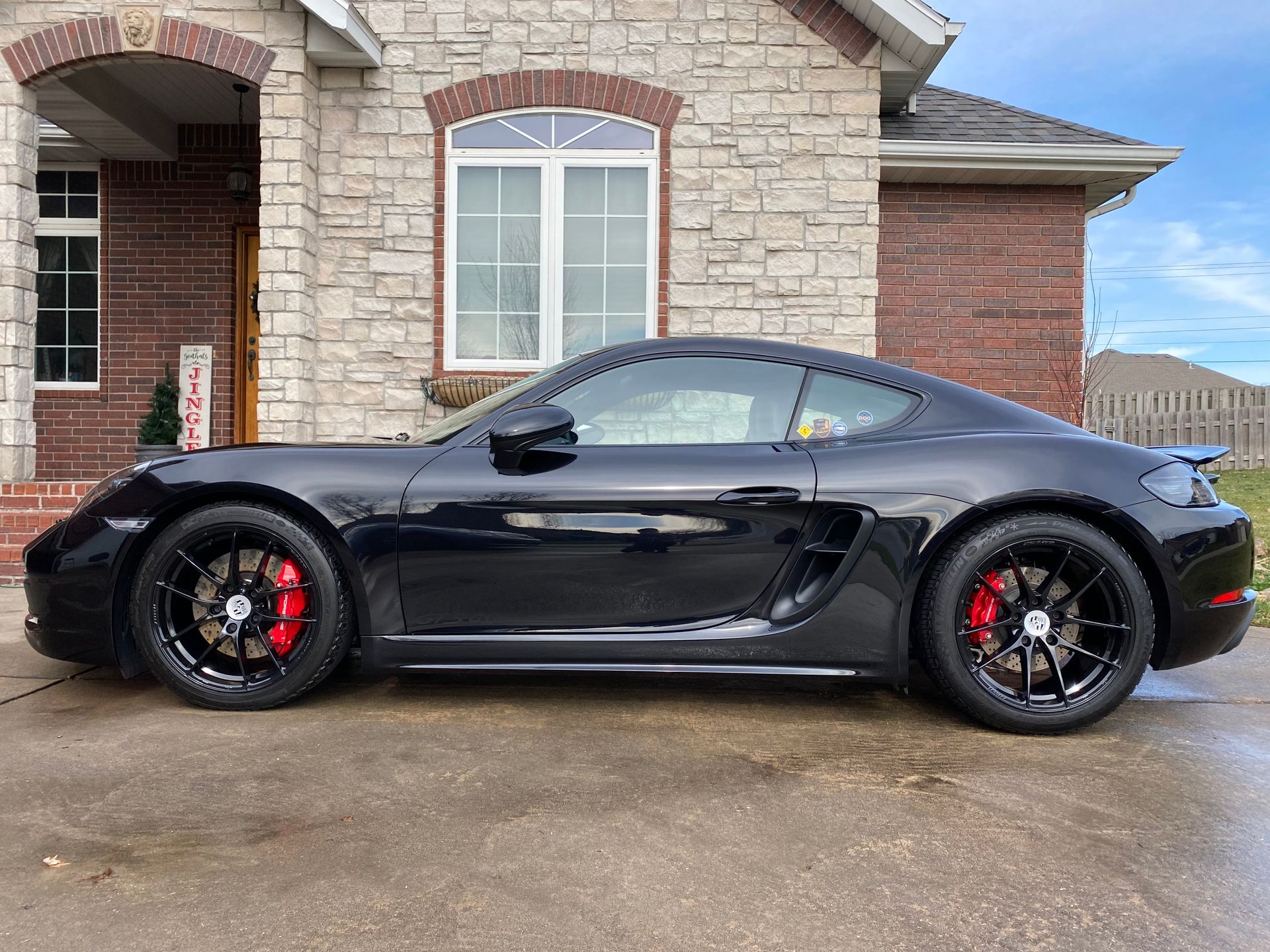 Black sports car parked in front of a stone house with brick accents
