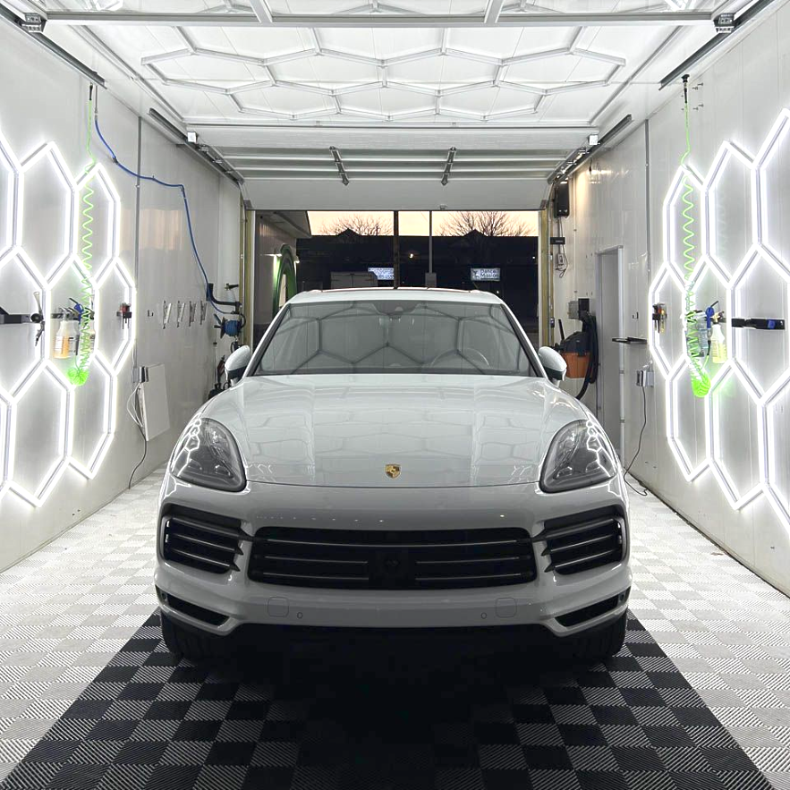 White SUV in a bright detailing bay with hexagonal lights on the walls and a checkered floor.