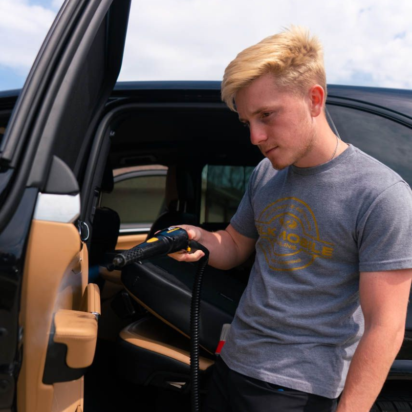 Man using a drill to remove a car door panel beside a black vehicle