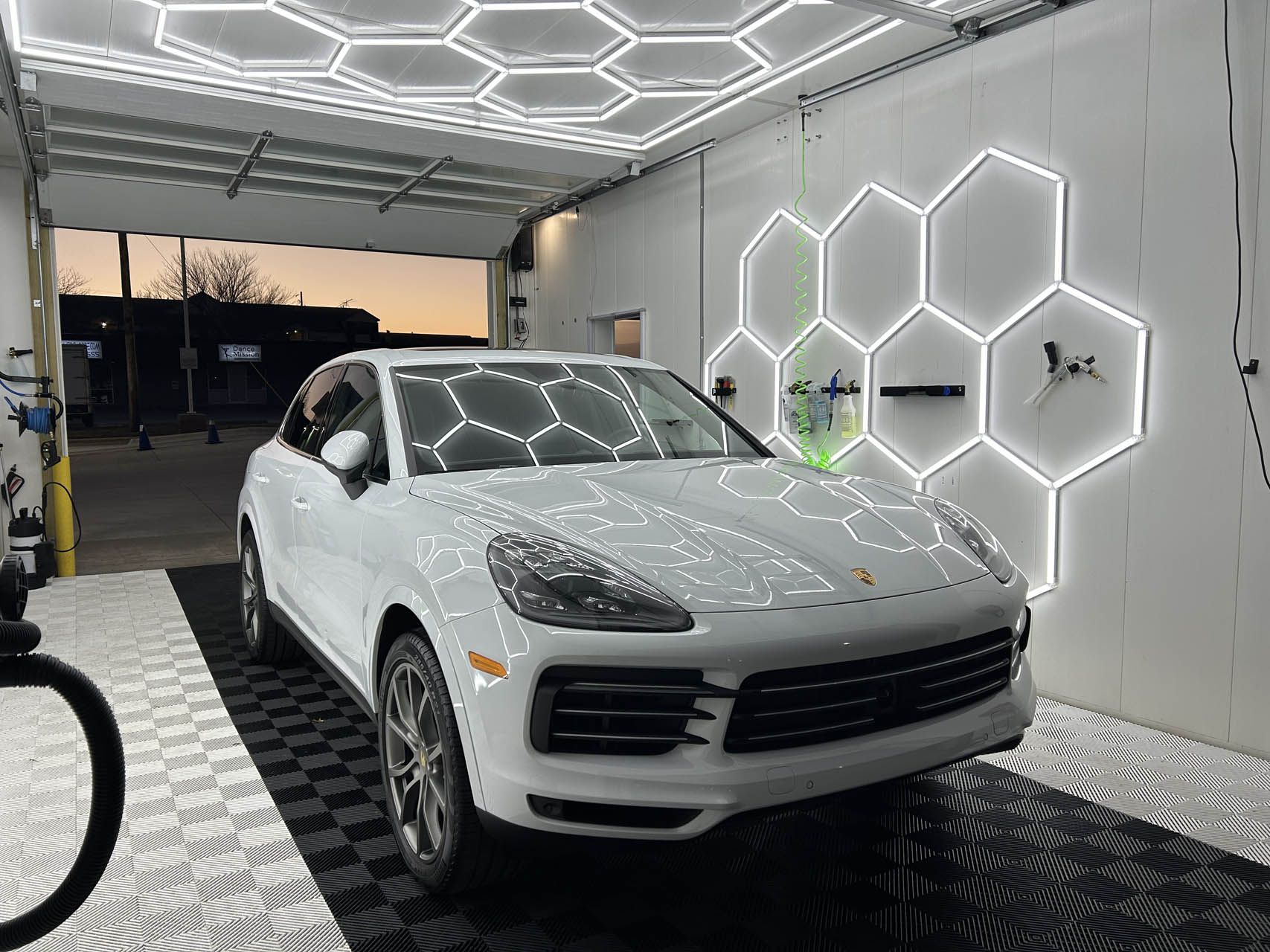 White SUV in a modern car wash bay with illuminated hexagon wall lights and wet floor mats