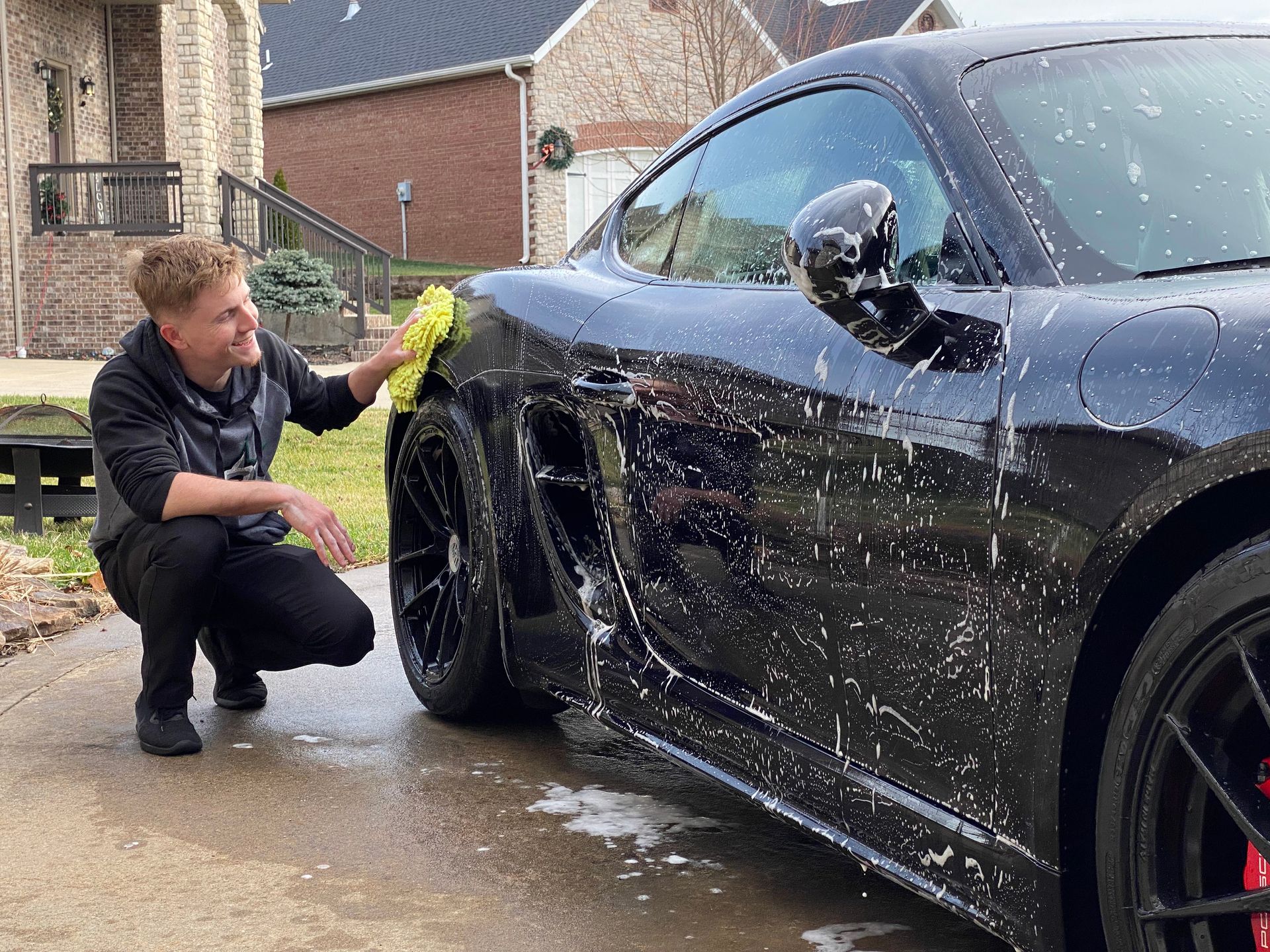 Person washing a black car with soap suds in a driveway