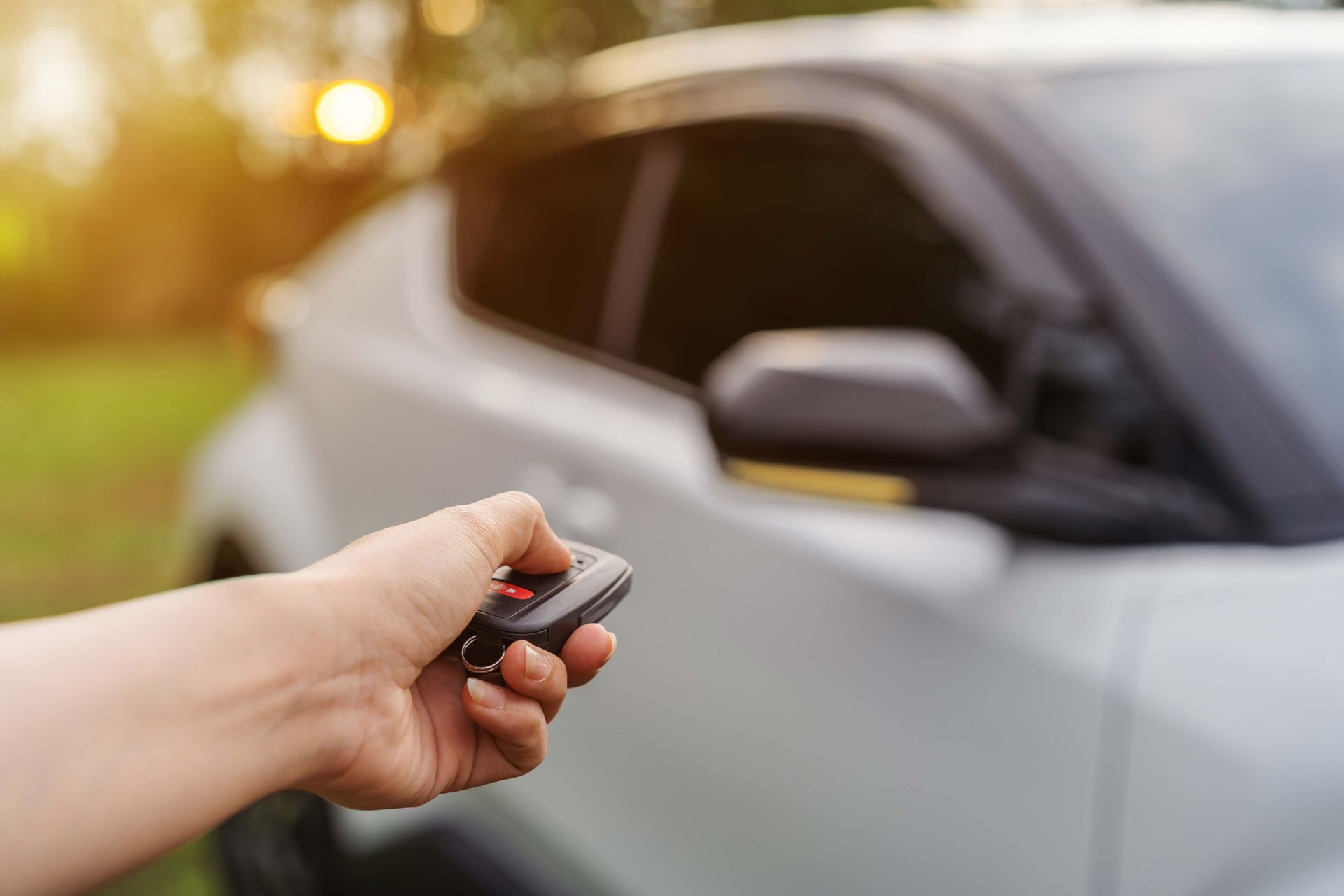Hand using car key remote to unlock a white car.