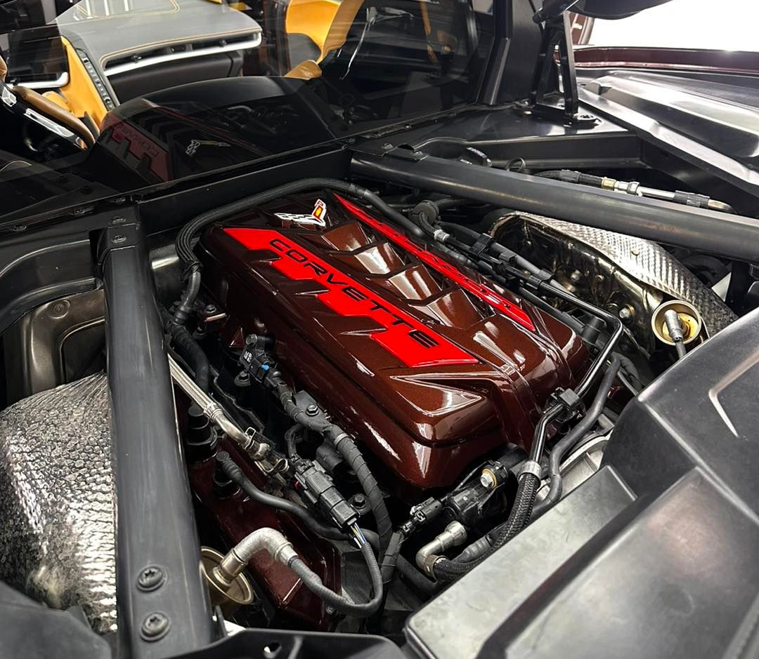 Close-up of a car engine bay, showing a maroon engine cover with red lettering.