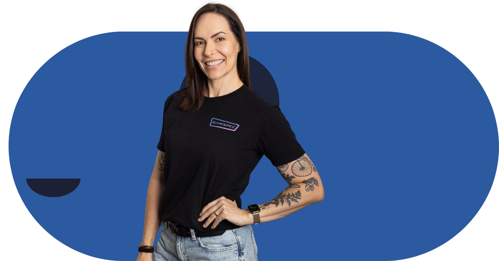 Woman in black T-shirt and jeans standing against a blue background with one hand on her hip