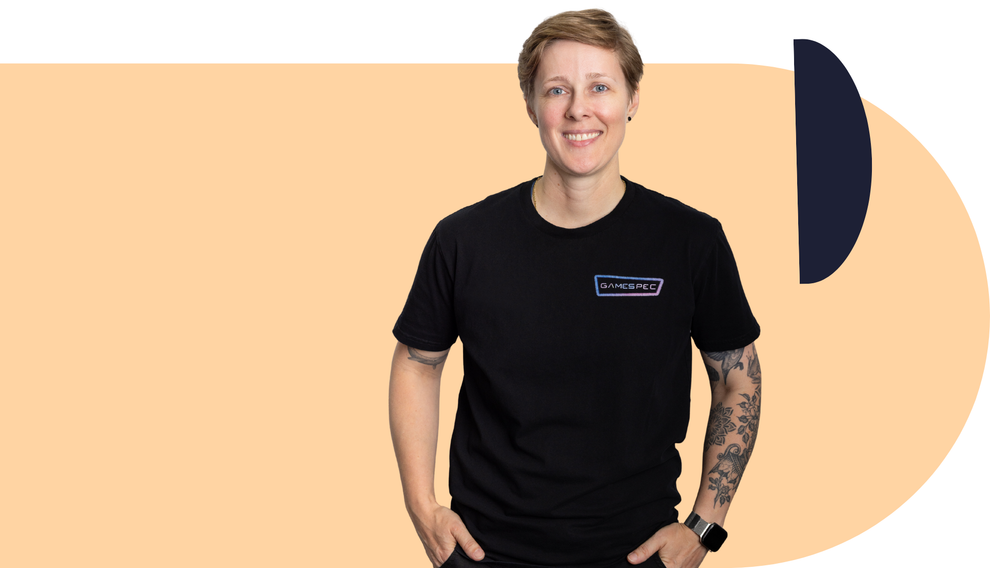 Person in black T-shirt standing against a peach background with a navy abstract shape.