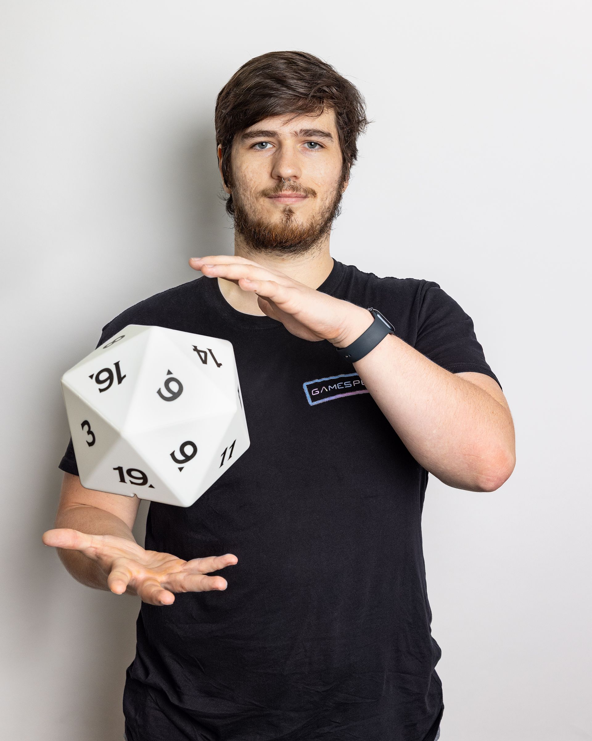 Person in a black shirt juggling a white 20-sided die against a plain background