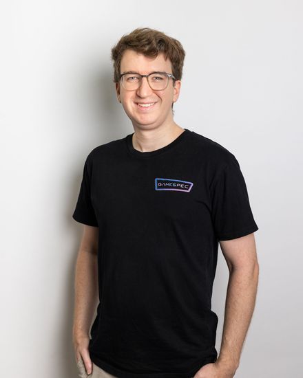 Smiling person in glasses wearing a black T-shirt against a light background