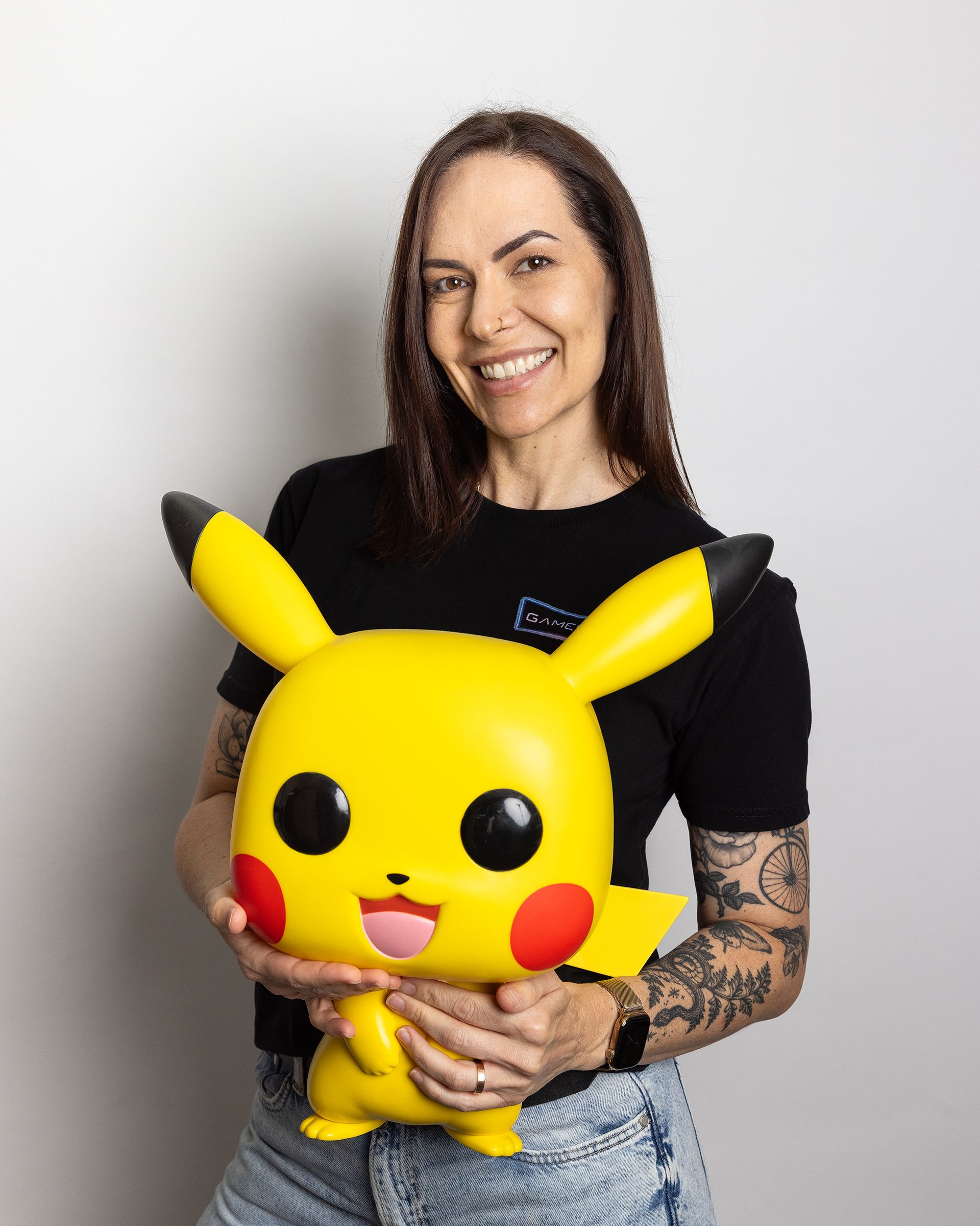 Woman holding a large yellow Pikachu plush, smiling against a plain light background.