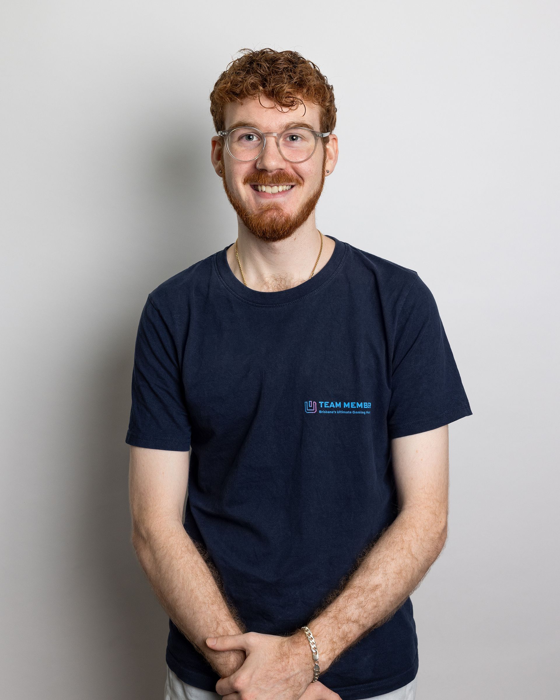 Smiling person with glasses in a navy T-shirt standing against a light gray background
