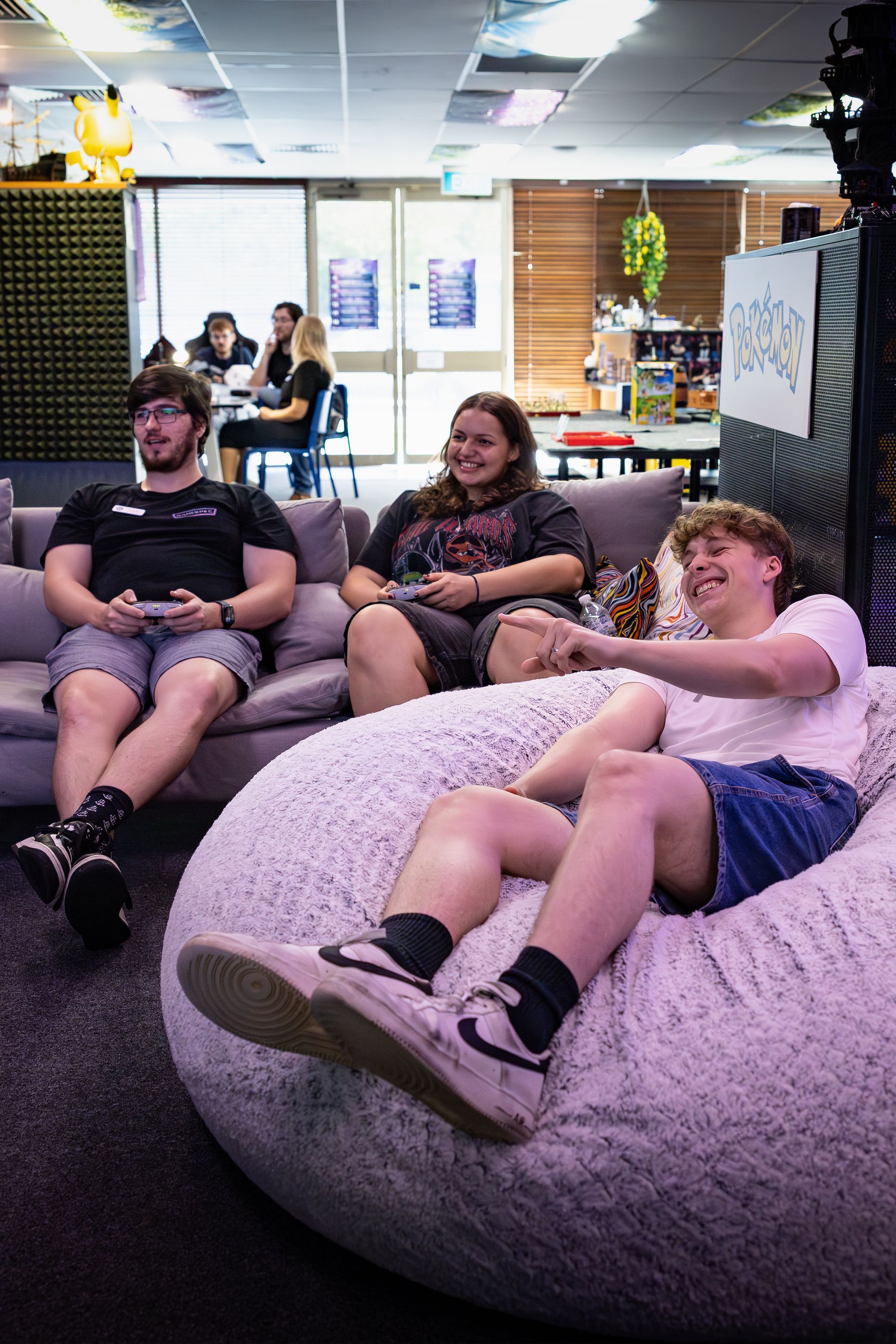 Three people relaxing on beanbags in a lounge, with one smiling and pointing at the camera.