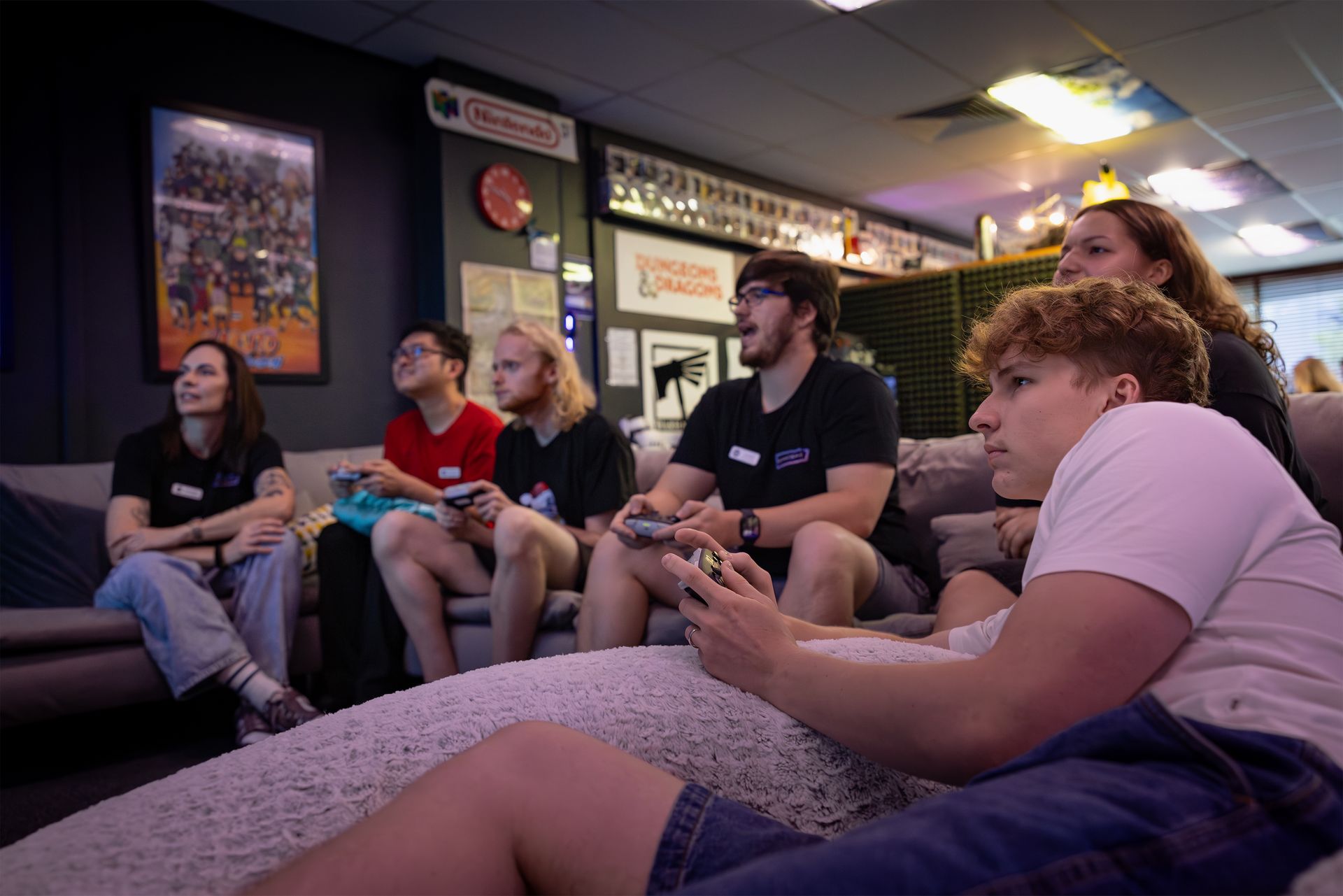 Group sitting in a living room, watching TV and holding game controllers.