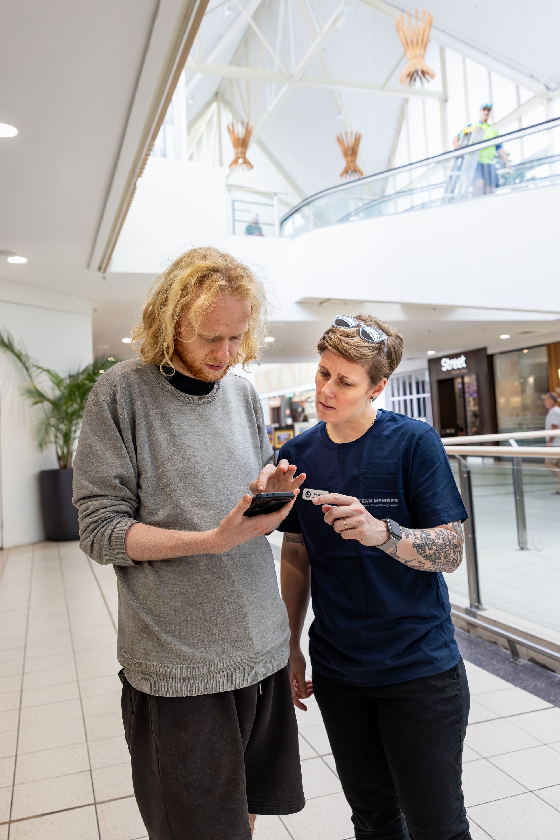 Two people standing in a bright atrium, looking at a smartphone together.