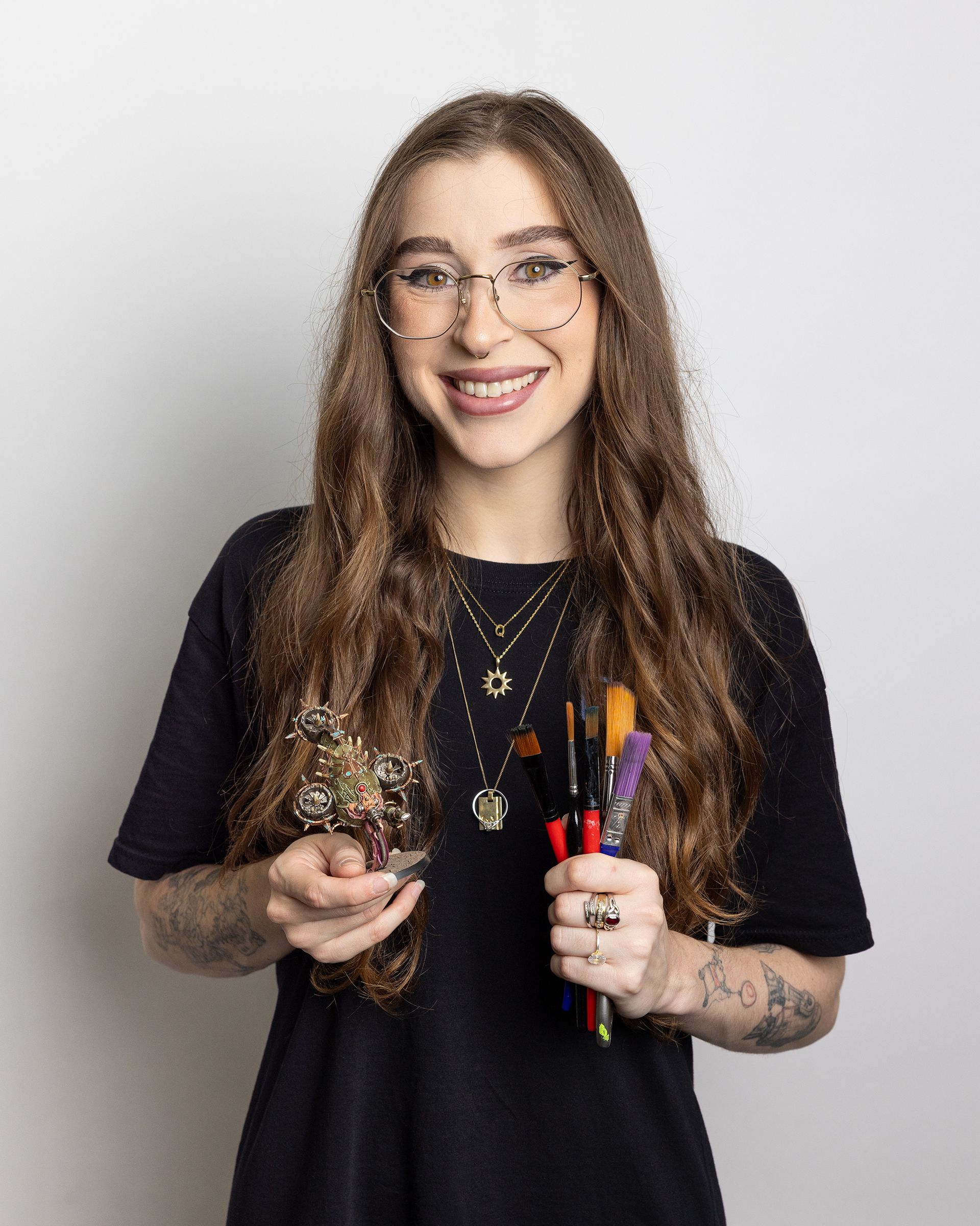 Smiling person holding paintbrushes and art supplies against a light background