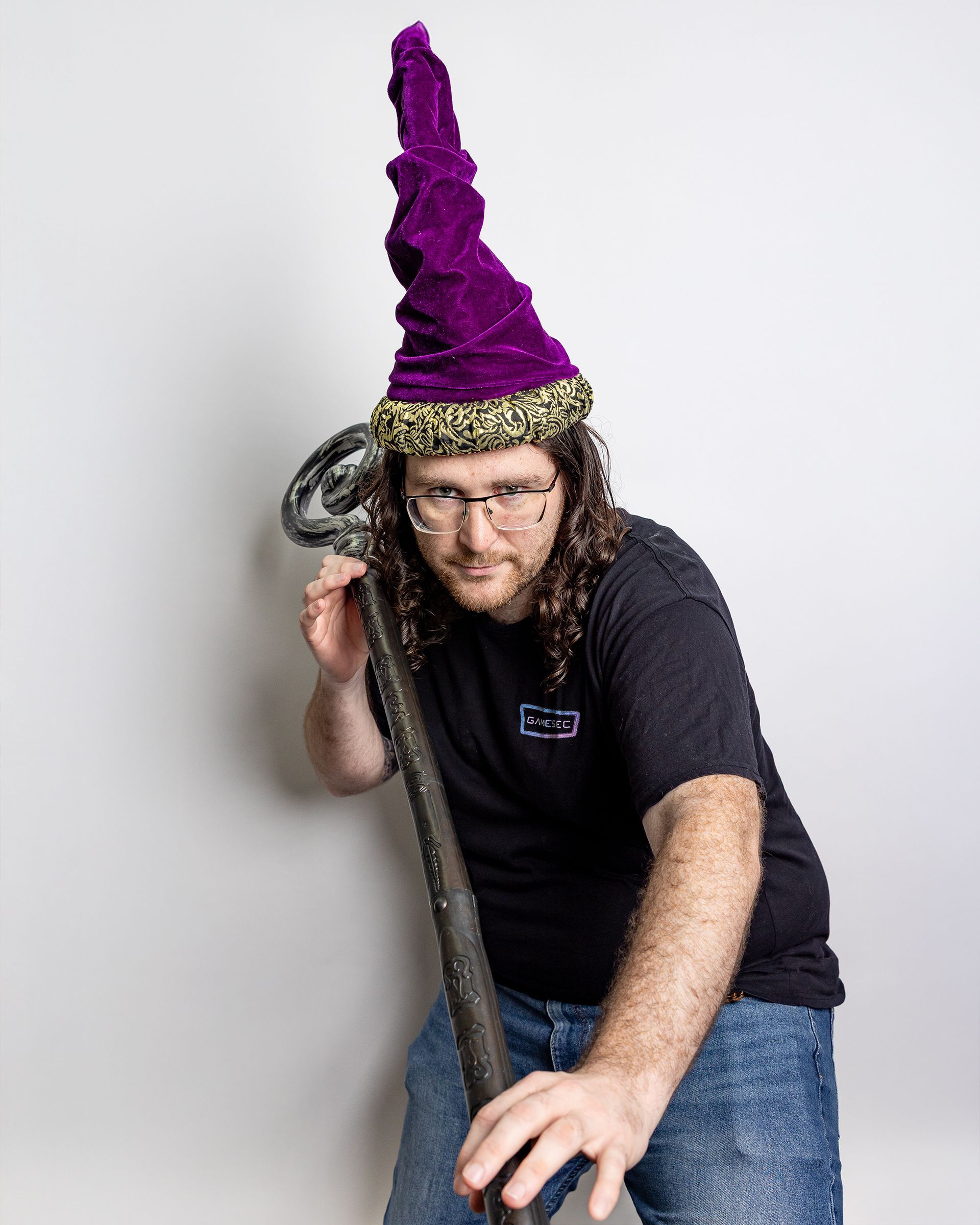 Person in a purple wizard hat, leaning on a broom-like staff against a plain background.