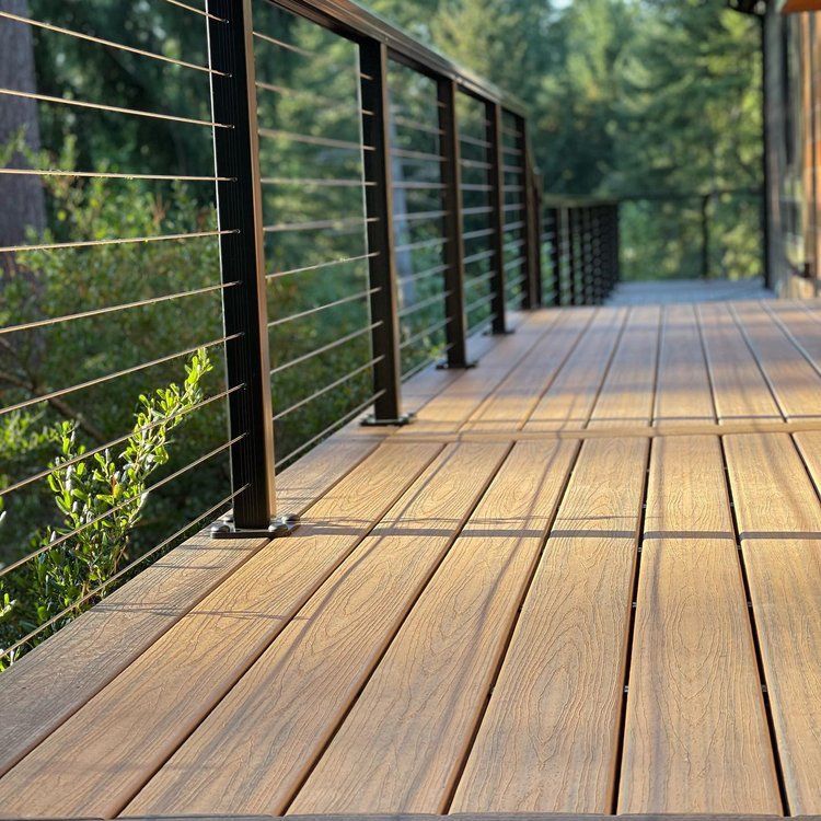 A wooden deck with a black railing and trees in the background.