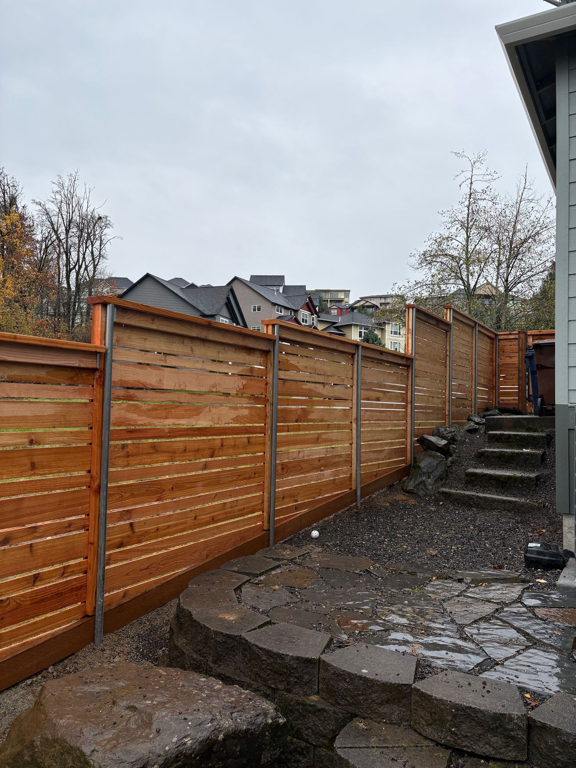 Wooden fence along a yard; cedar planks, metal posts, gravel path, overcast sky.