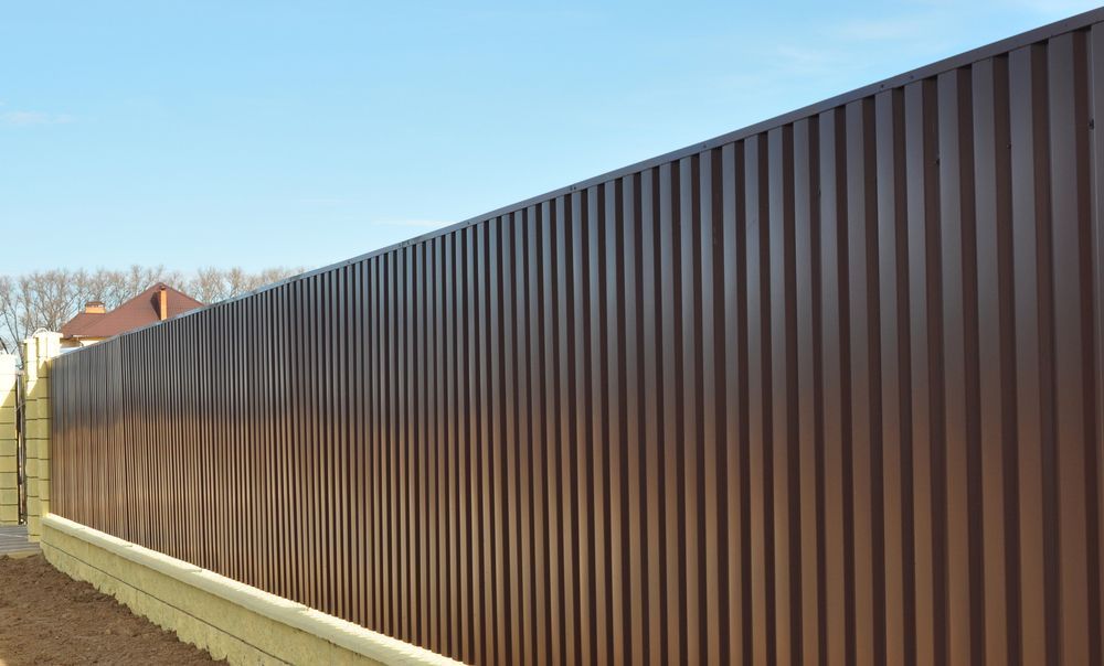 Long Brown Metal Fence Along a Residential Yard on A Sunny Day — My Handyman Townsville In Garbutt, QLD