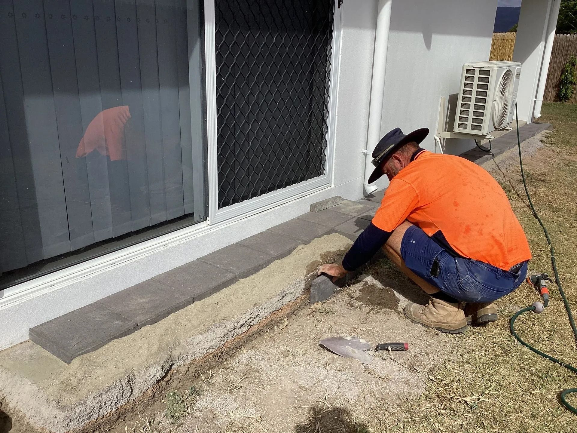 Person in a Hat, Using a Trowel to Work on a Trench Next to a Building — My Handyman Townsville In Garbutt, QLD