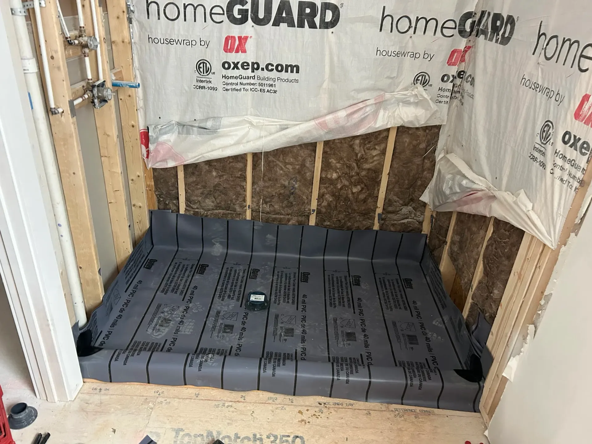 Shower stall under construction, featuring a gray waterproof membrane base, wooden studs, and insulation.