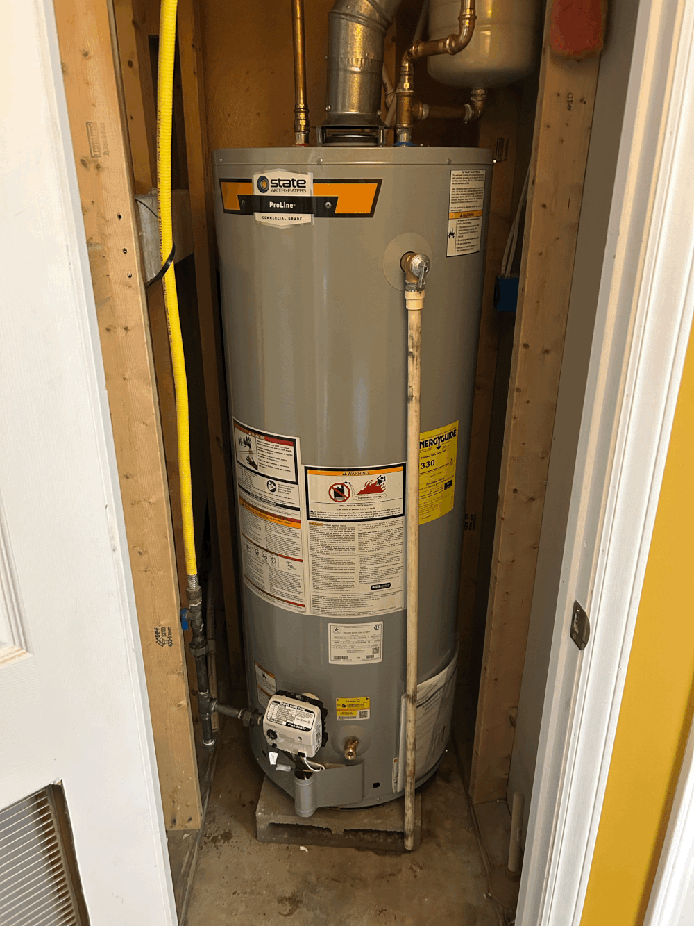A tall, gray water heater sits in a tight space between wooden studs. Yellow gas line.