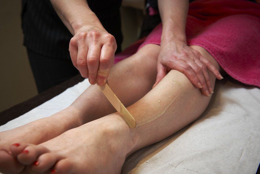 Beautician applying wax to female's leg to remove hair