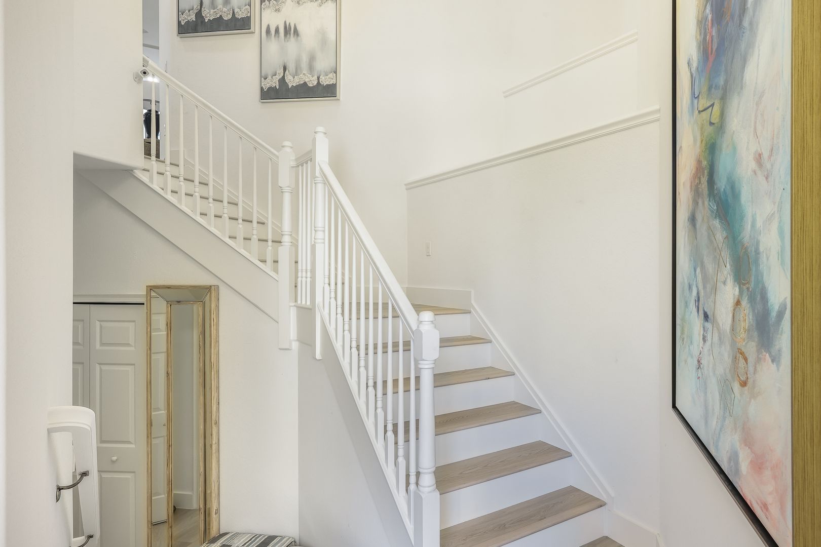 A staircase in a house with a white railing and a painting on the wall.
