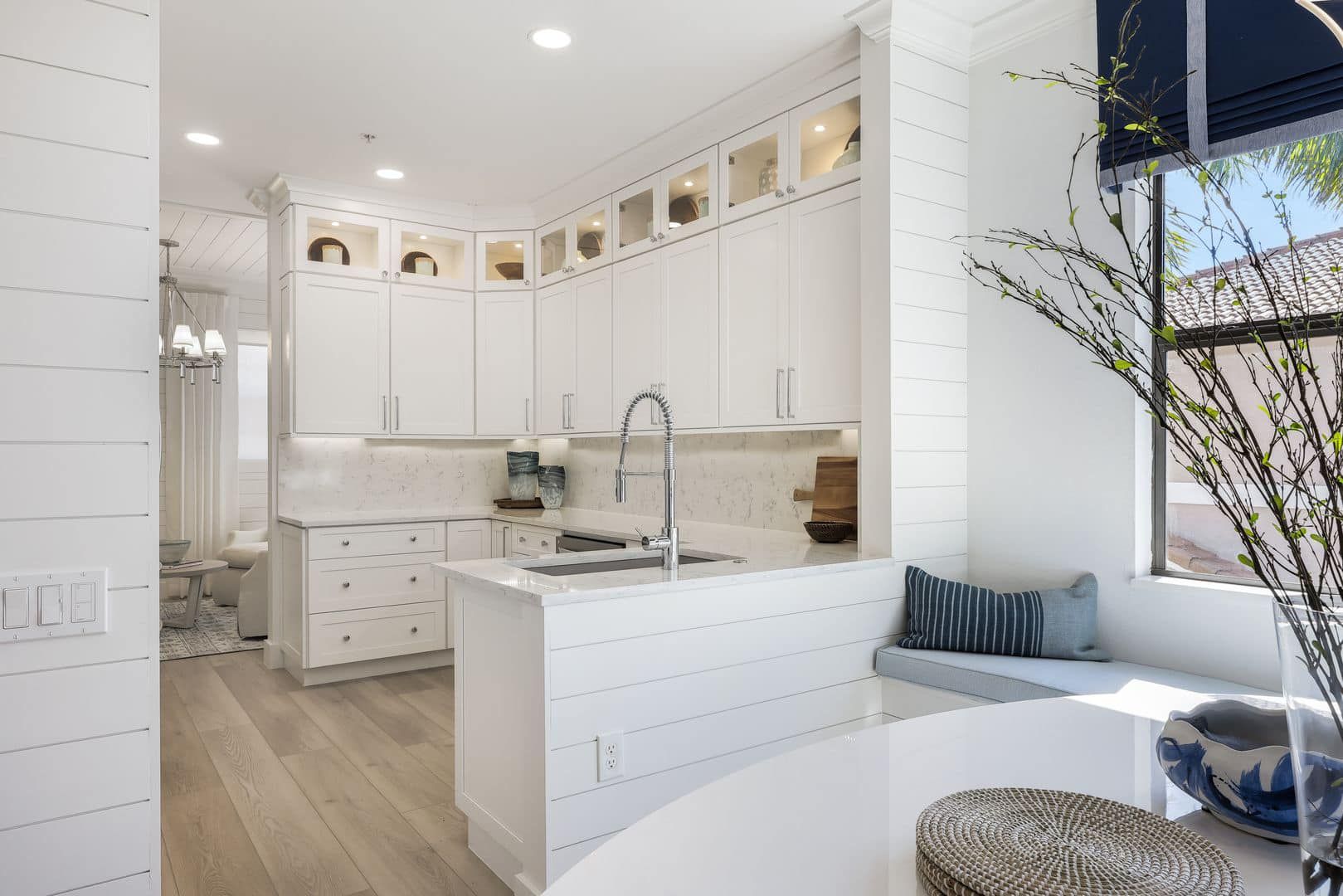 A kitchen with white cabinets , a sink , and a window seat.