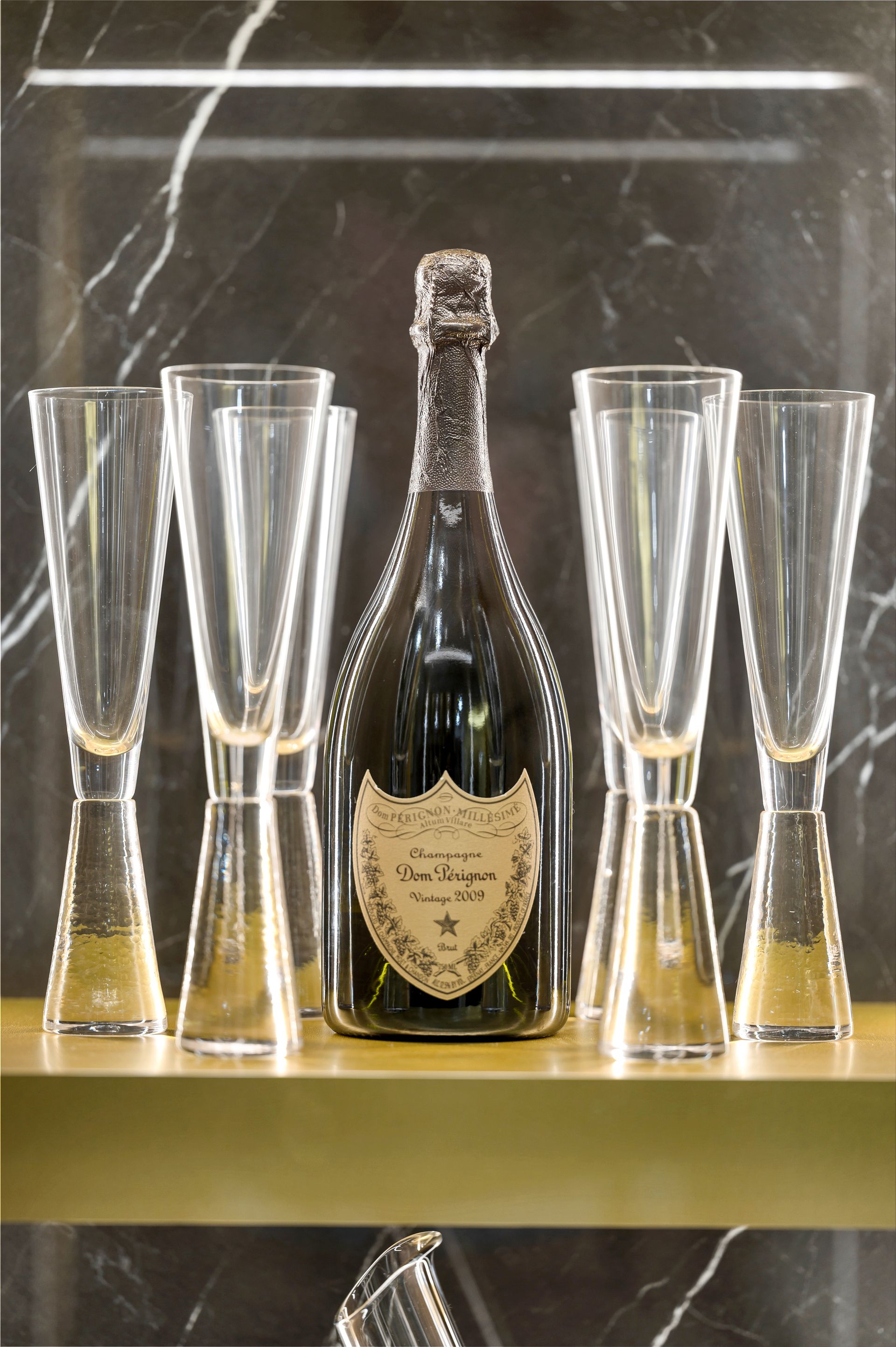 A bottle of champagne sits on a shelf next to empty champagne flutes.
