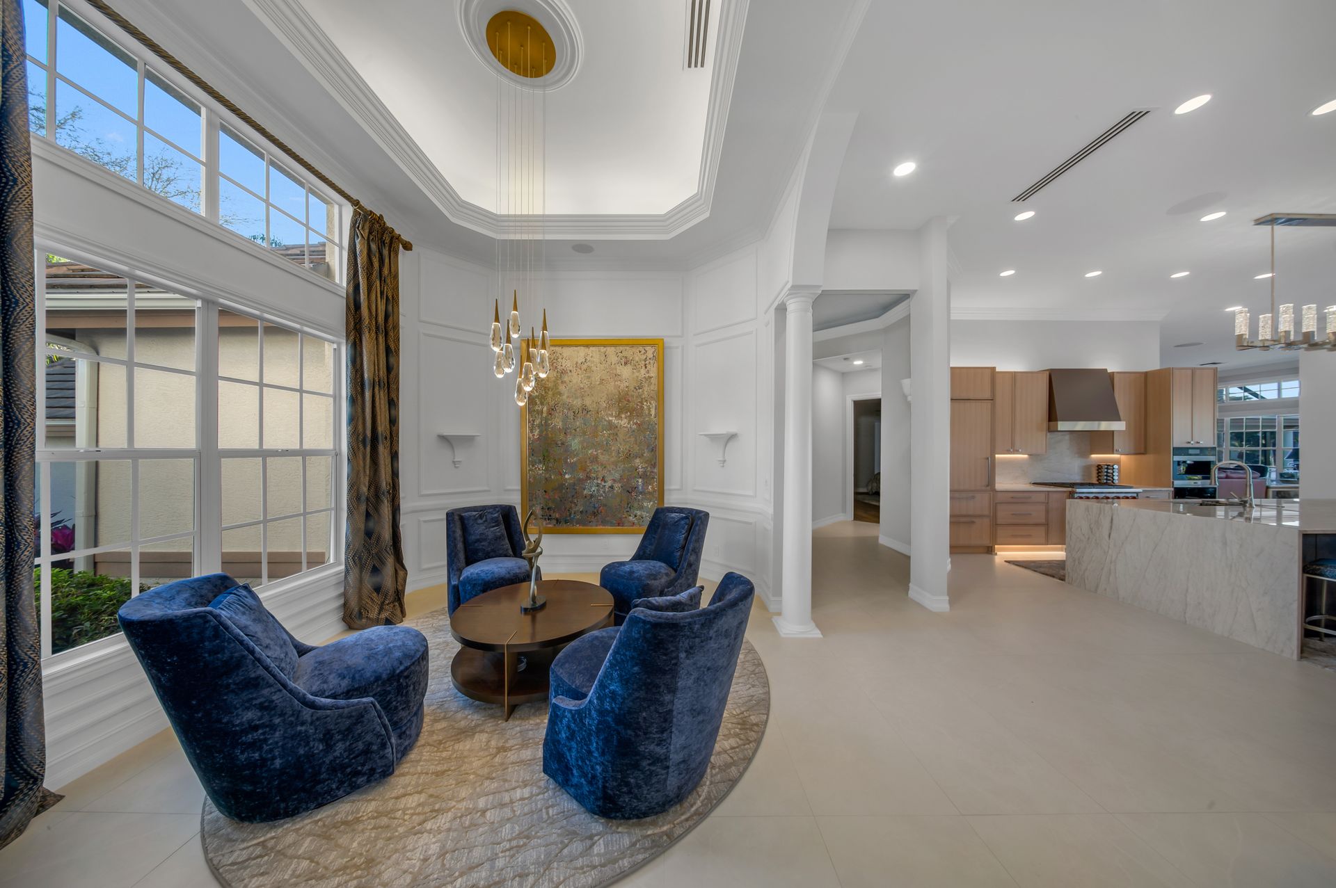 A living room with blue chairs , a coffee table , and a painting on the wall.