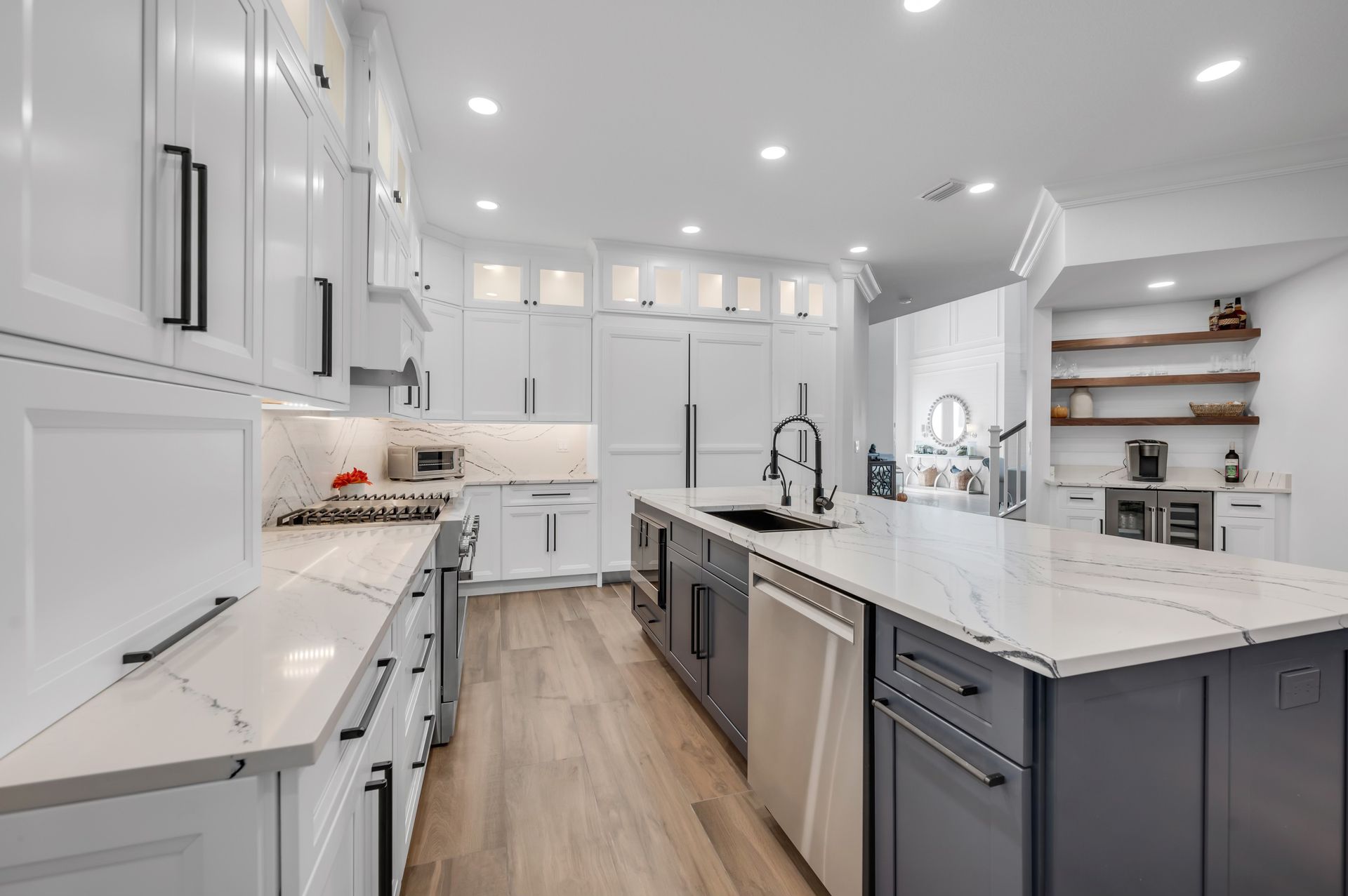 A kitchen with white cabinets and gray cabinets and a large island in the middle.