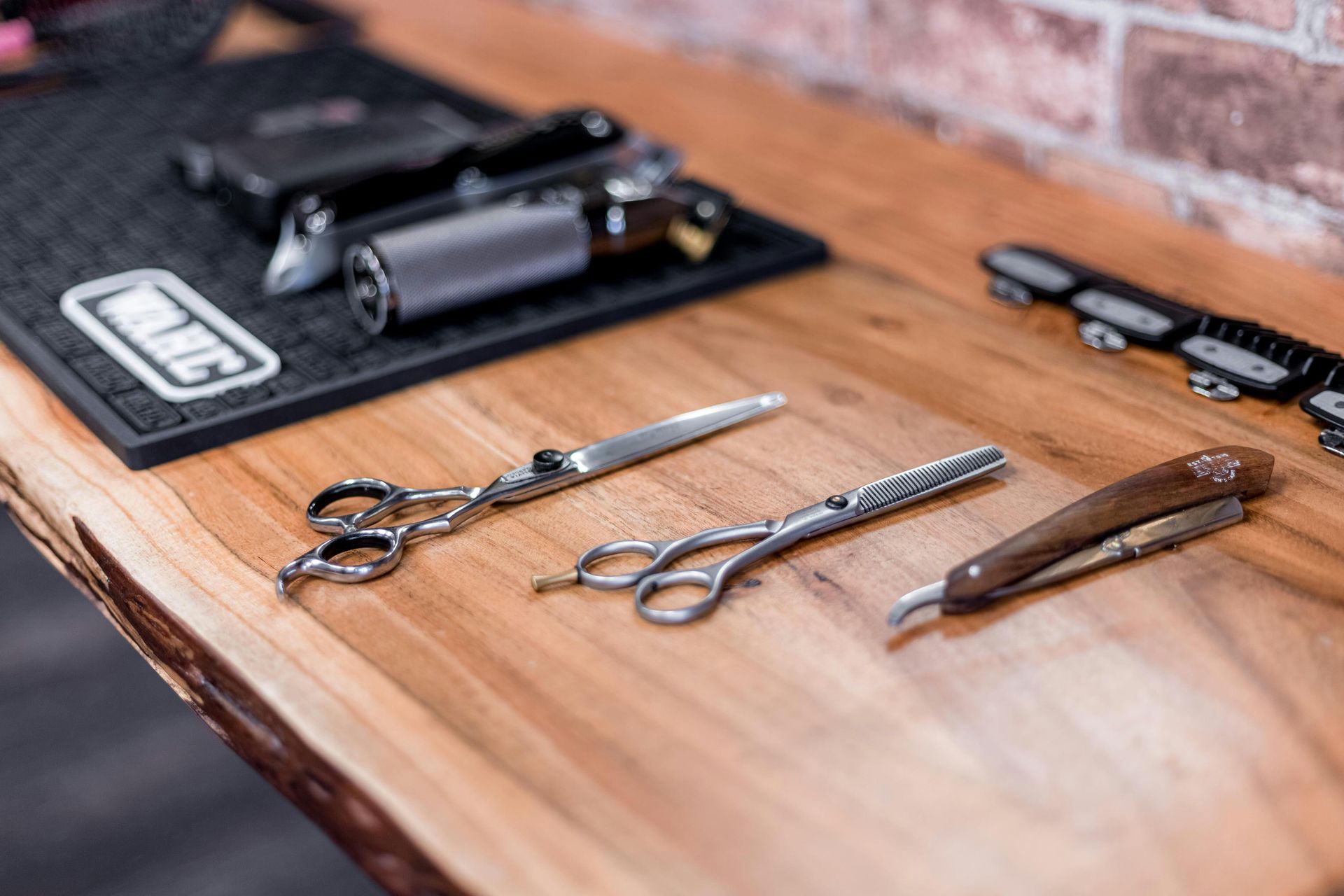 Scissors and a straight razor on a wooden barber counter, with clippers in the background