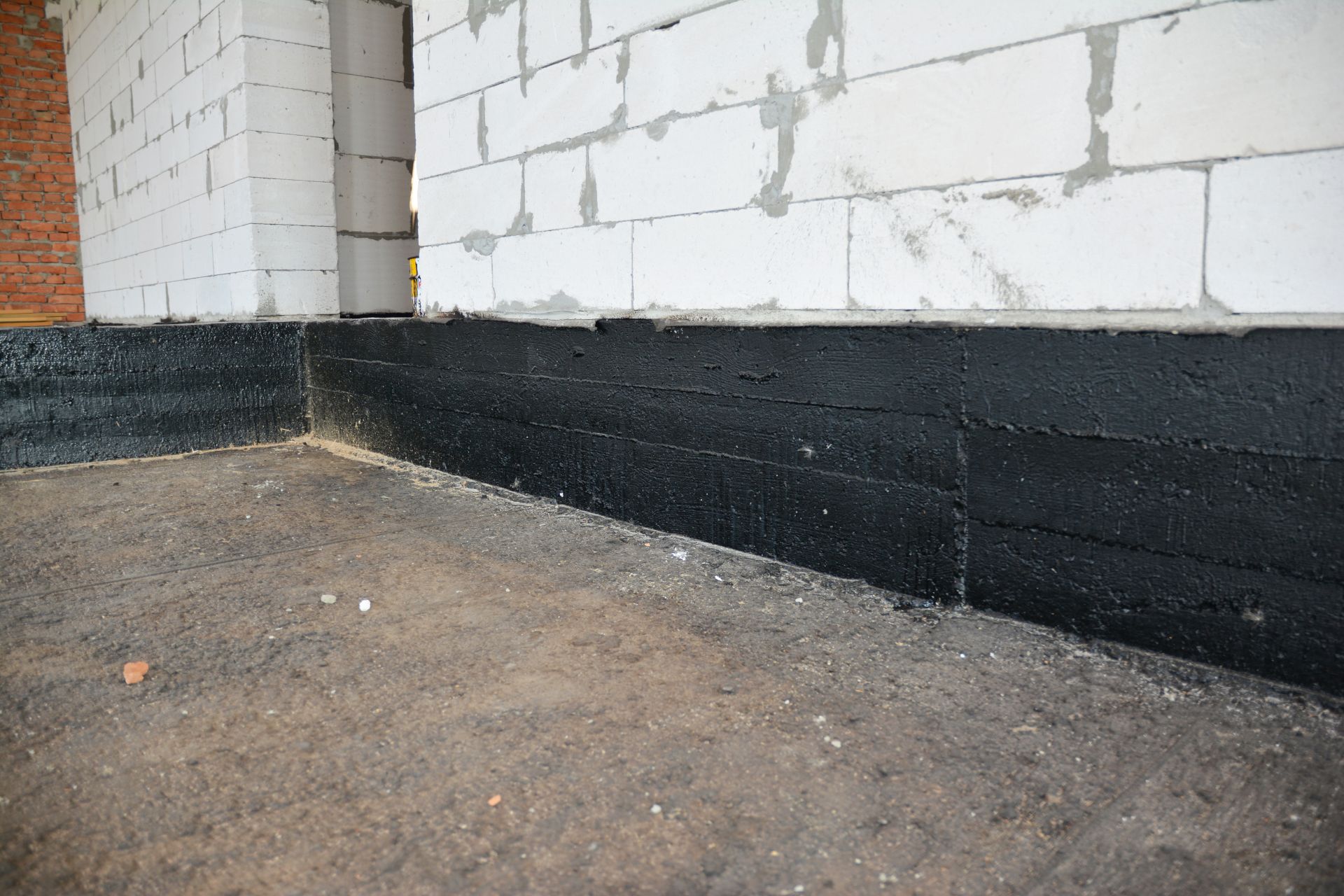 Black waterproofed foundation wall beside unfinished white brick exterior at ground level