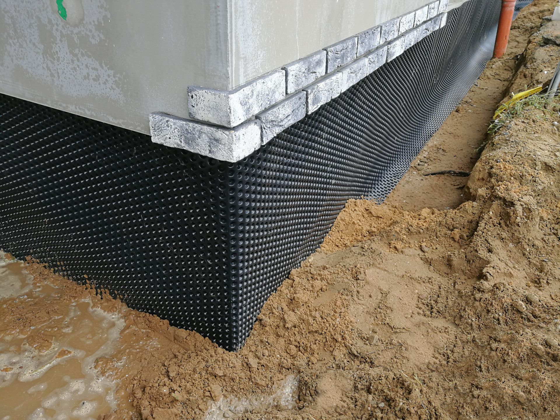 House foundation with black waterproofing membrane and gravel trench around the base