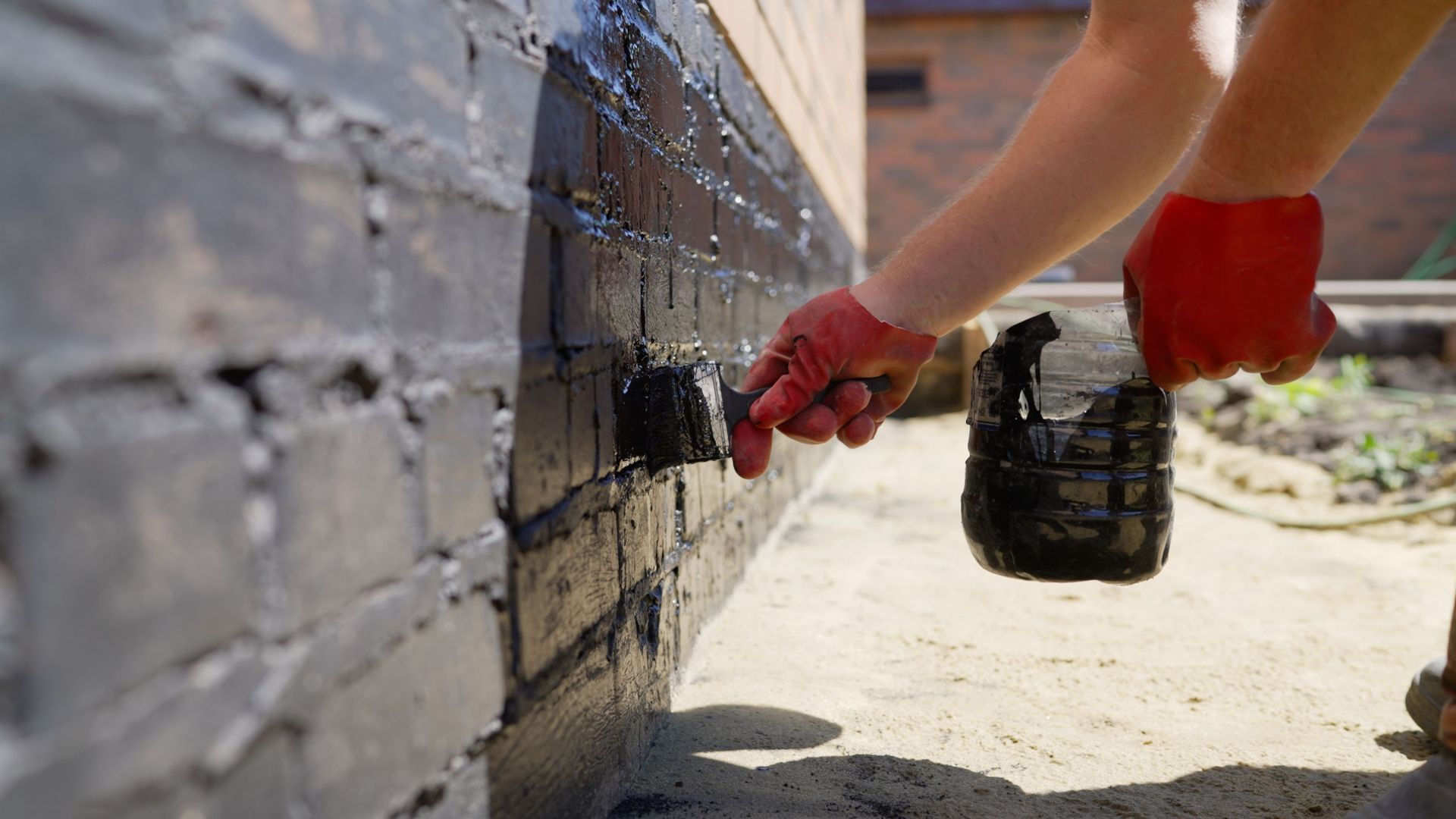 Person painting a brick wall with a small brush and black paint outdoors