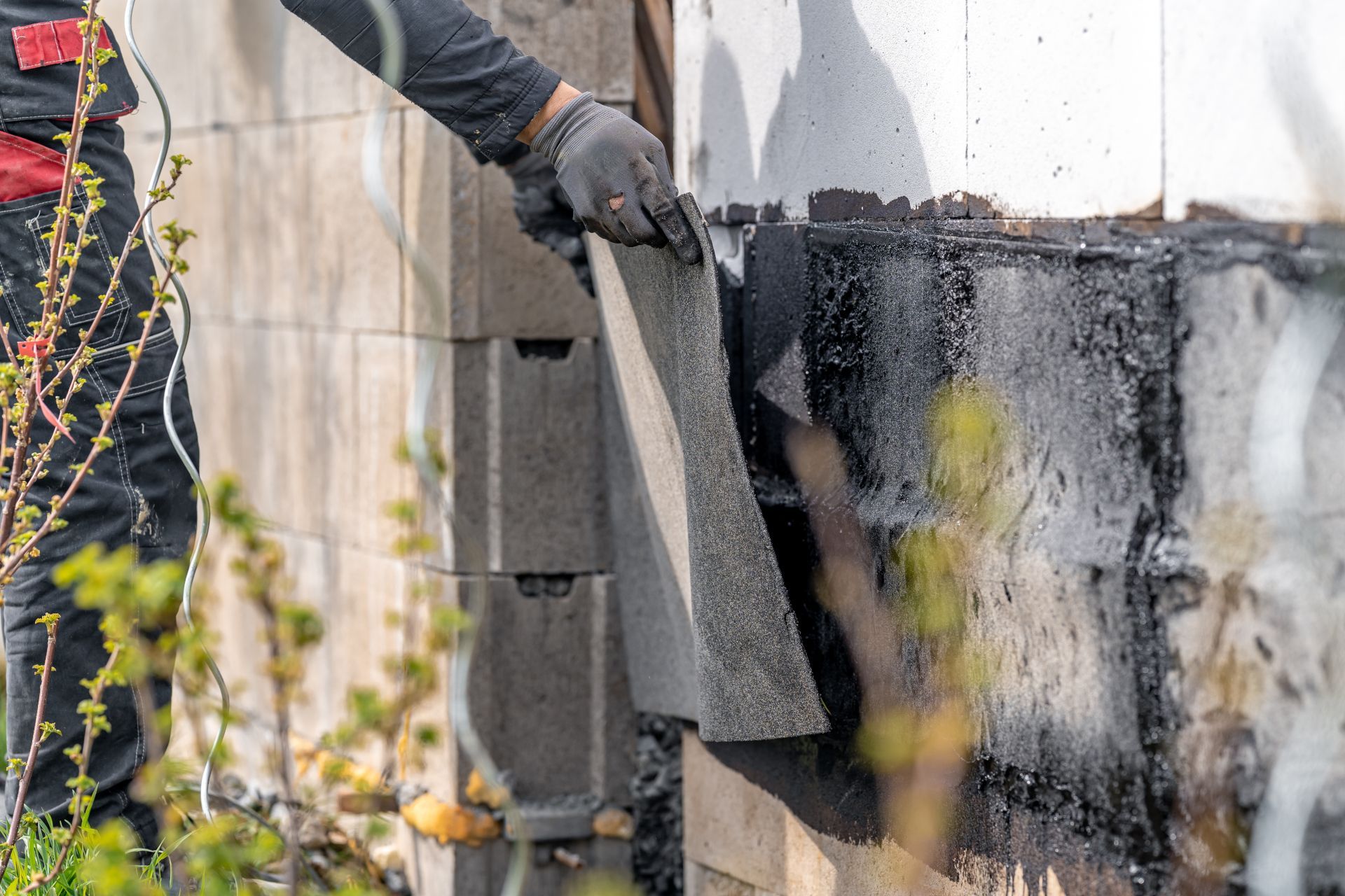 Gloved worker peeling black waterproof membrane from an outdoor wall during repairs