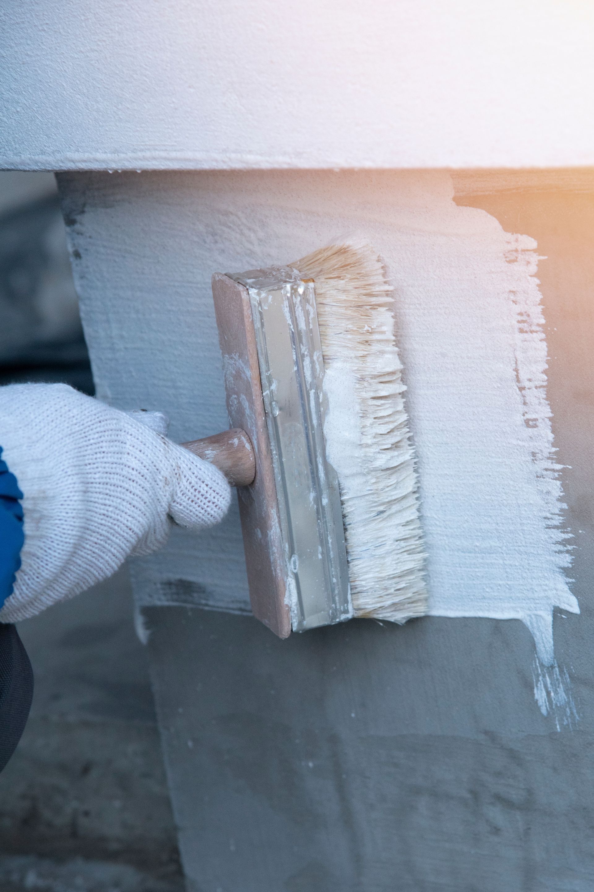 Gloved hand applying gray sealant to a wall with a brush near a seam
