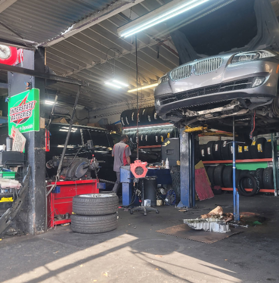 Auto repair shop with a car raised on a lift, mechanic working underneath, and tires stacked nearby