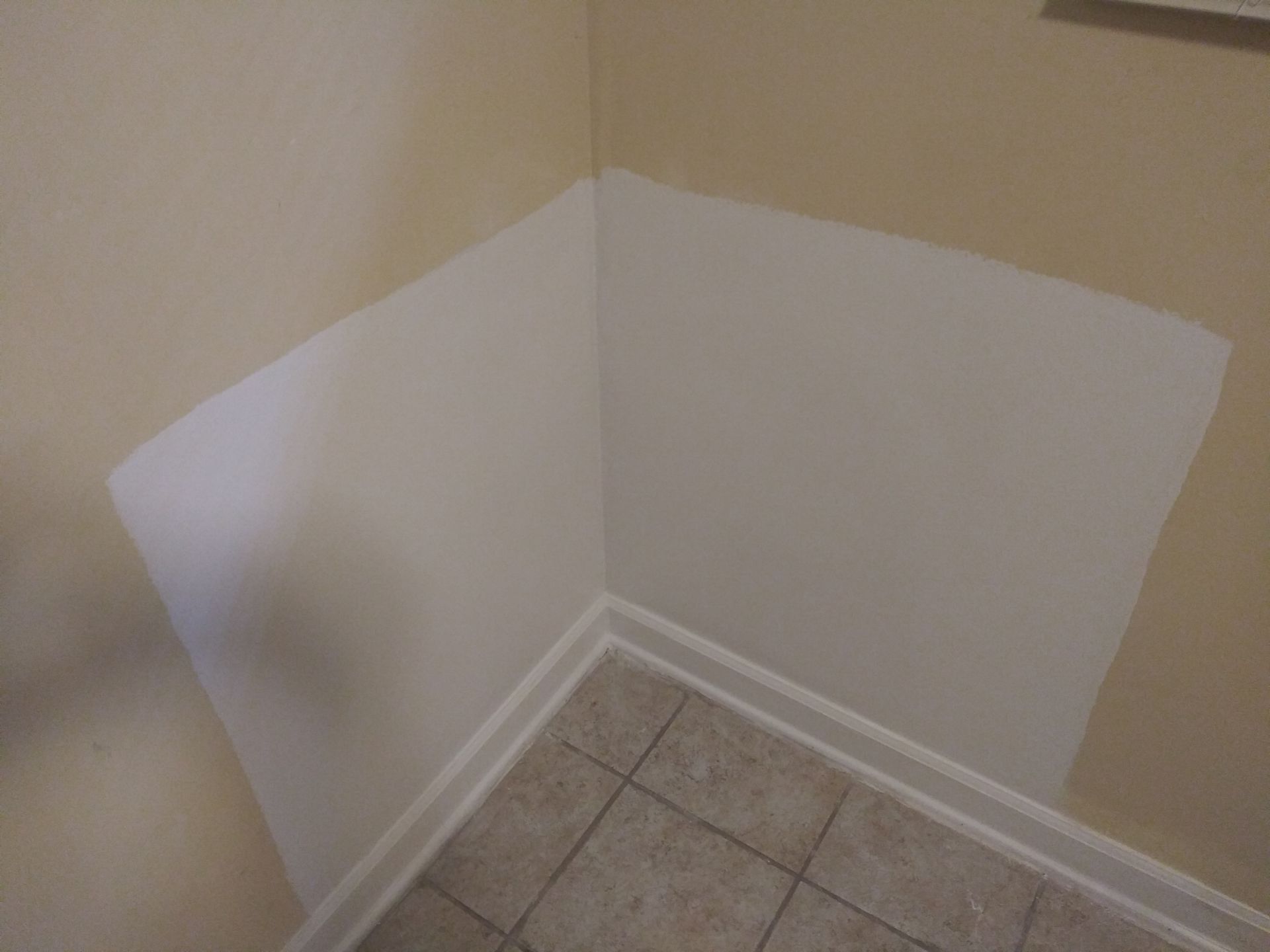 A corner of a room with a white wall and tile floor.